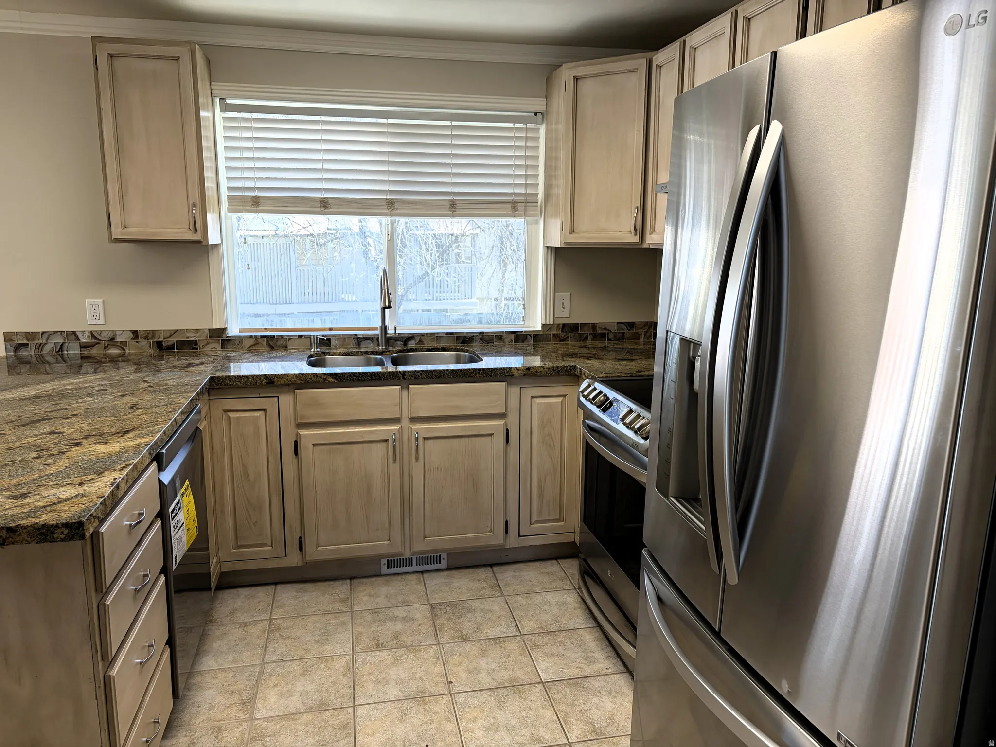 Kitchen featuring stainless steel appliances, dark stone counters, light wood finish cabinetry, and crown molding