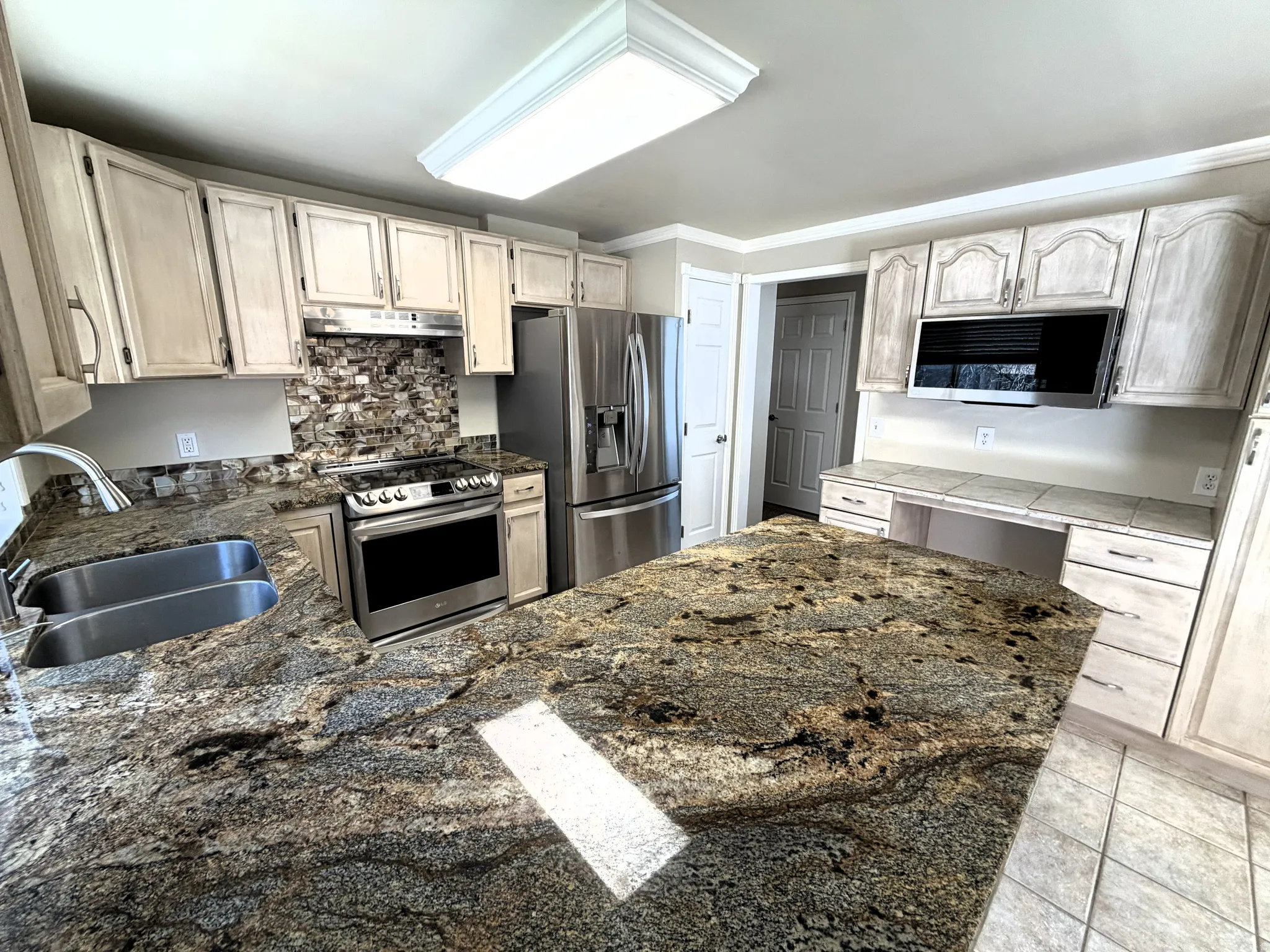 Kitchen featuring stainless steel appliances, decorative backsplash, light tile patterned floors, a peninsula, and dark stone counters