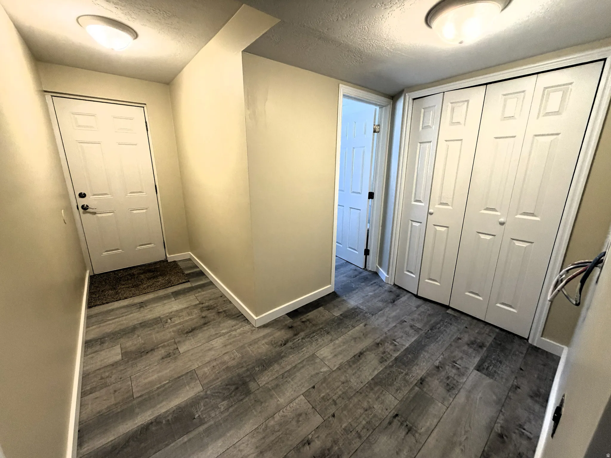Corridor featuring a textured ceiling and dark wood finished floors bathroom entrance and rear basement walkout