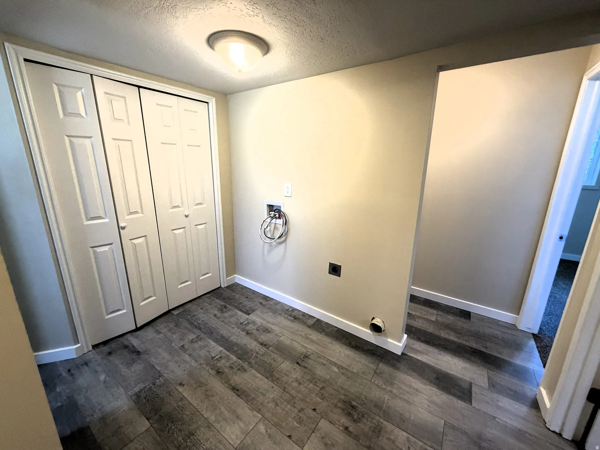 Laundry area with a textured ceiling, hookup for a washing machine, electric dryer hookup, and dark wood-style floors. Utility closet for water heater and furnace.
