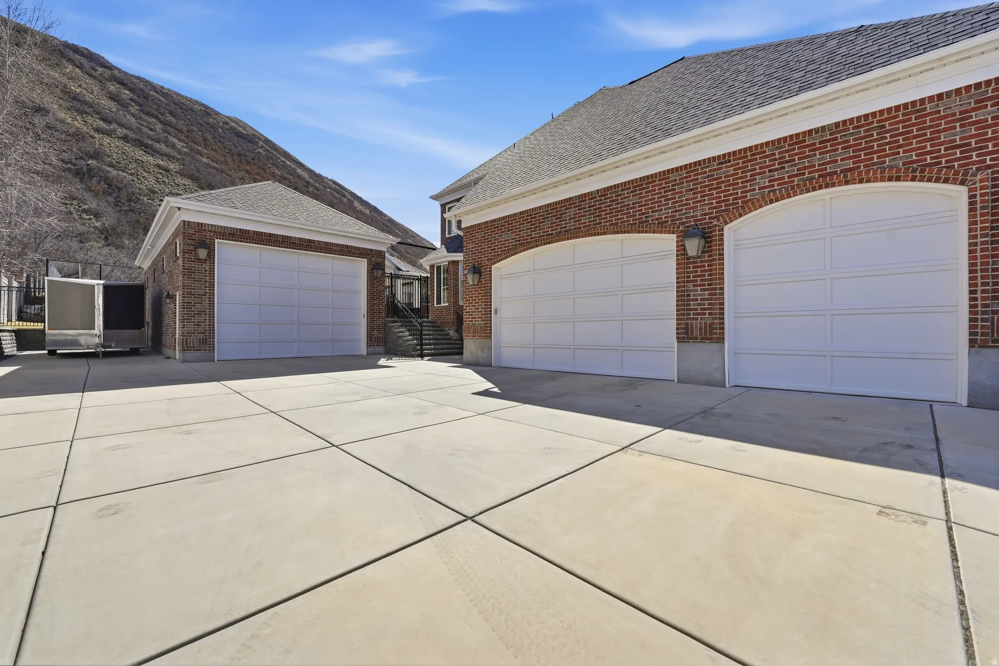 View of side of property featuring a shingled roof, driveway, brick siding, and an outbuilding