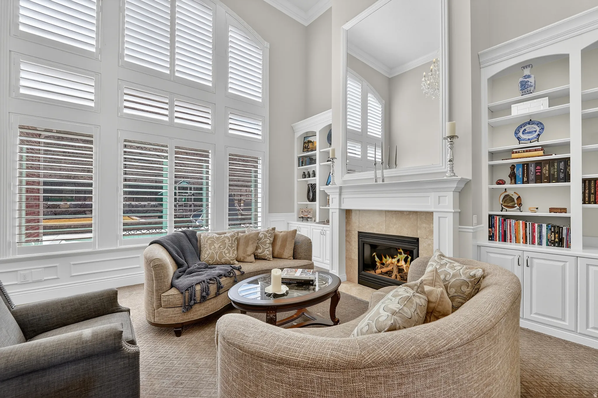 Living area with built in shelves, carpet flooring, a tiled fireplace, ornamental molding, and a high ceiling