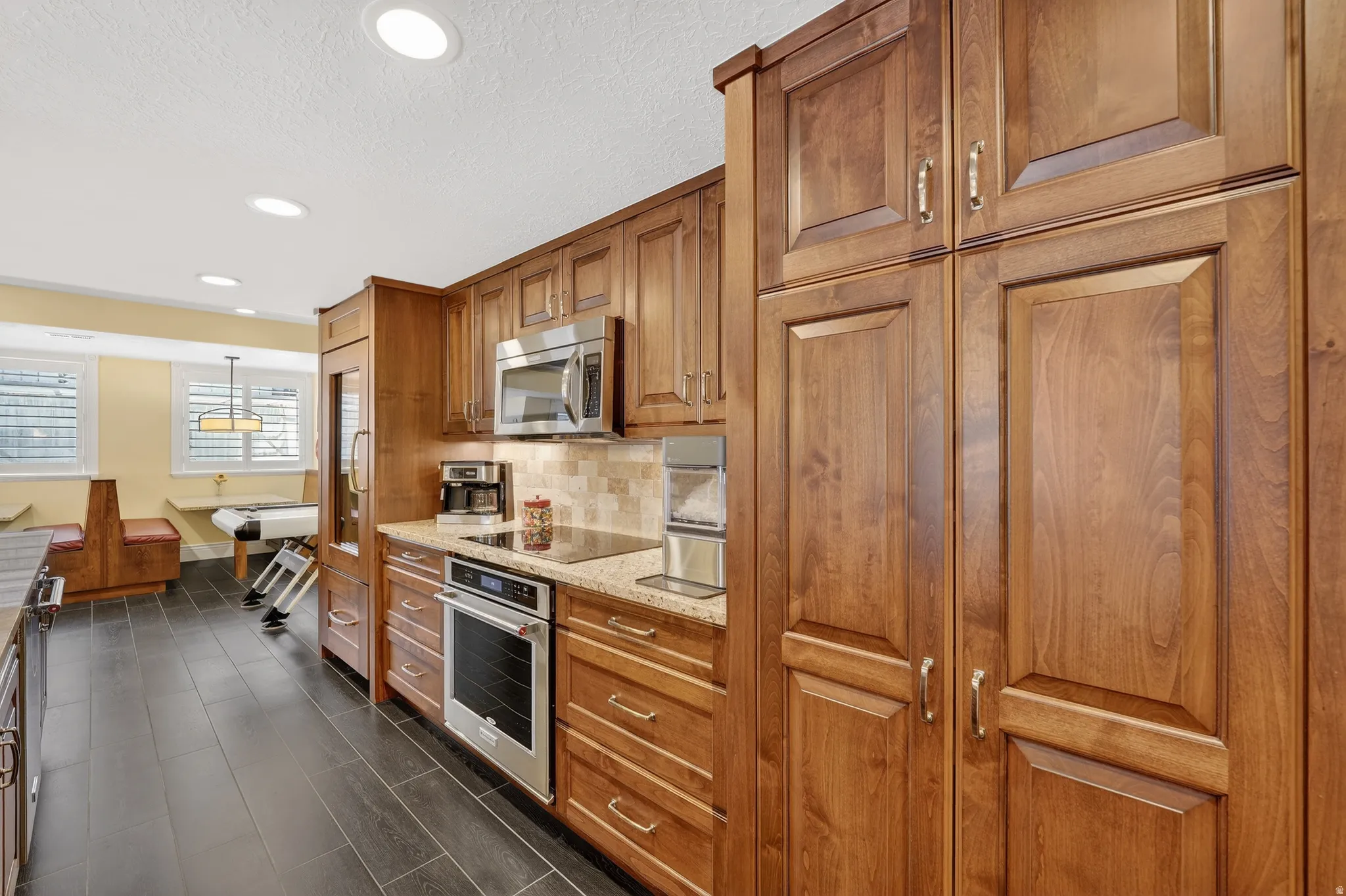 Kitchen featuring wood finish cabinetry, light stone countertops, stainless steel appliances, decorative backsplash, and hanging light fixtures