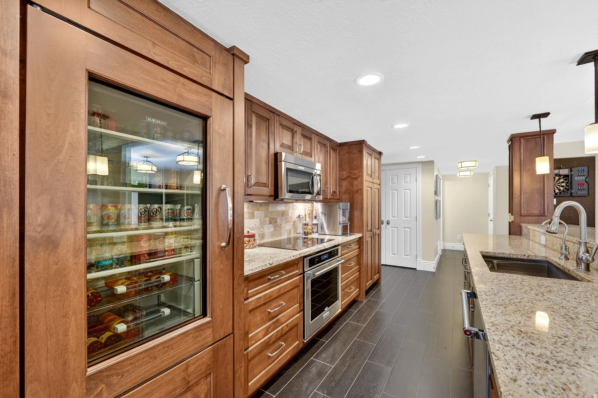Kitchen featuring light stone countertops, pendant lighting, stainless steel appliances, wood finish cabinetry, and tasteful backsplash