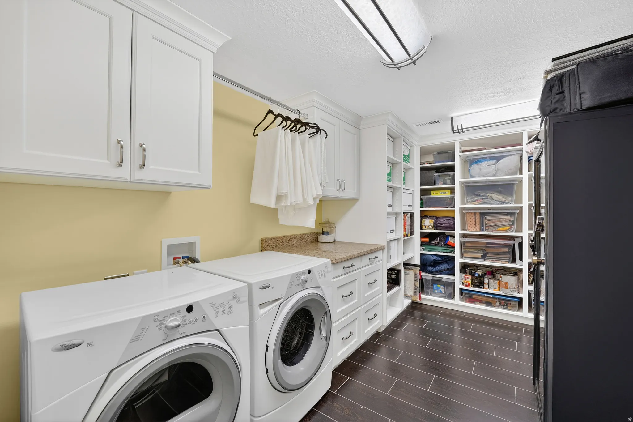 Laundry room with a textured ceiling, independent washer and dryer, cabinet space, and wood finish floors