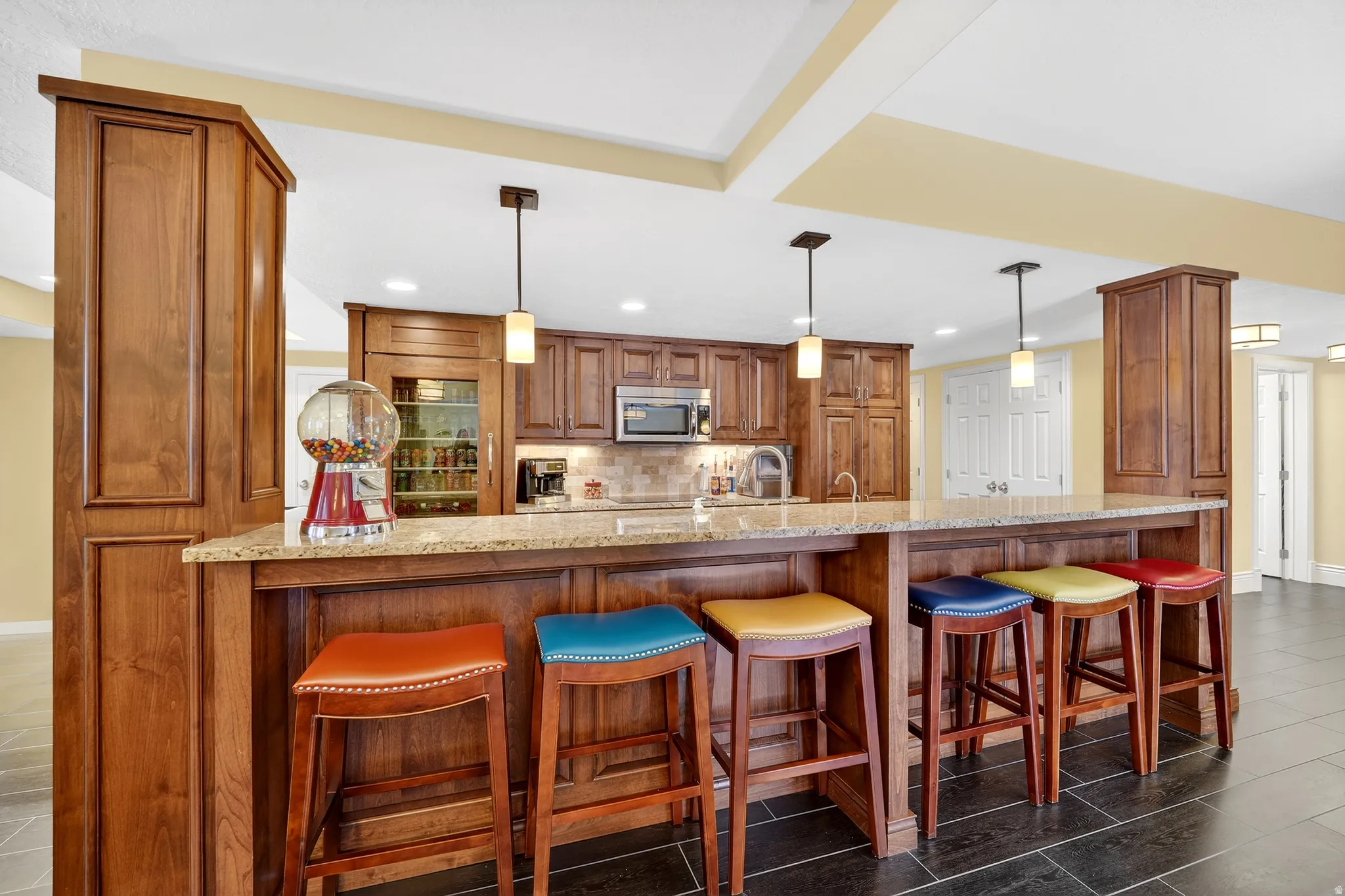 Kitchen with wood finish cabinetry, a breakfast bar area, a peninsula, light stone counters, and pendant lighting