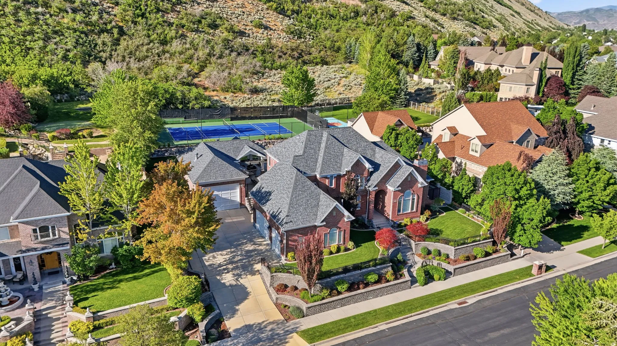 Brick-clad residence featuring a multi-car driveway, tiered landscaping, and an integrated tennis court