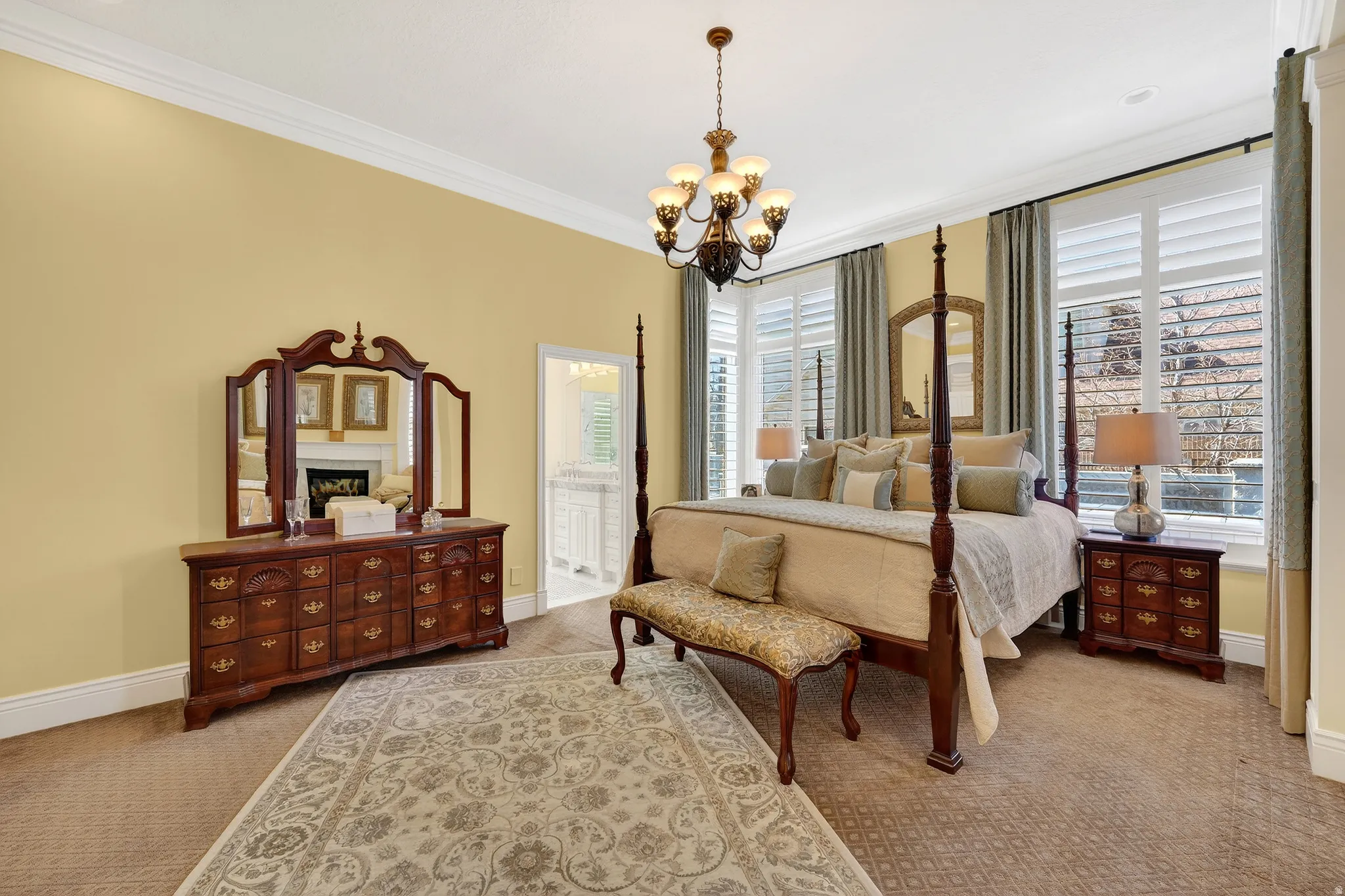Bedroom with ornamental molding, hanging lights, light carpet, multiple windows, and ensuite bath
