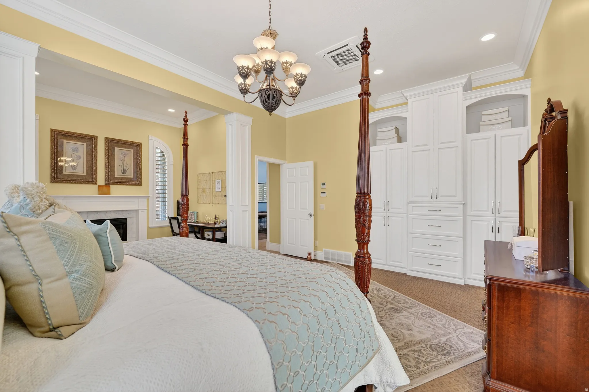 Bedroom with carpet flooring, a fireplace, hanging lights, decorative columns, and crown molding