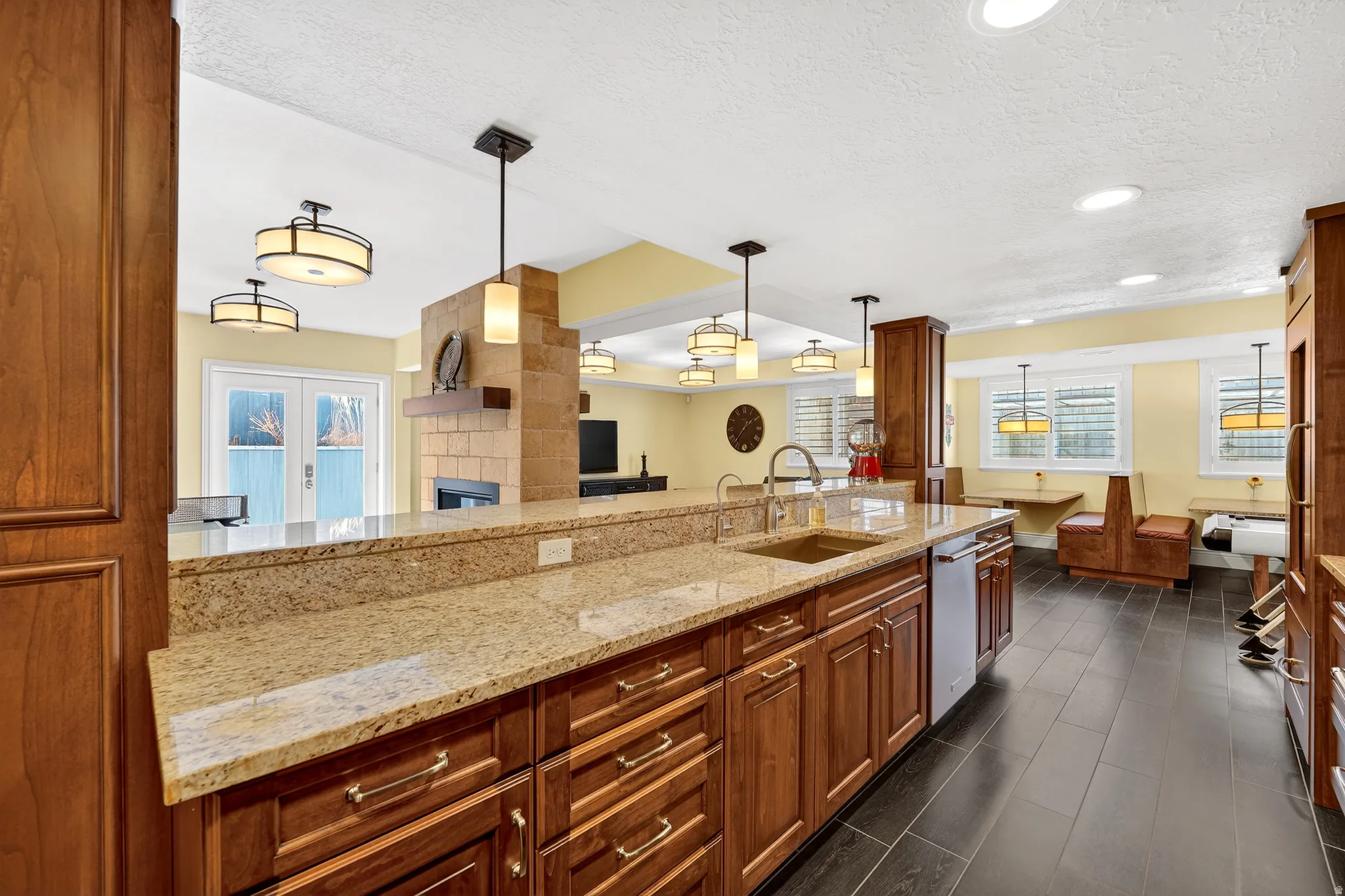 Kitchen with wood finish cabinetry, light stone counters, hanging light fixtures, a fireplace, and a textured ceiling