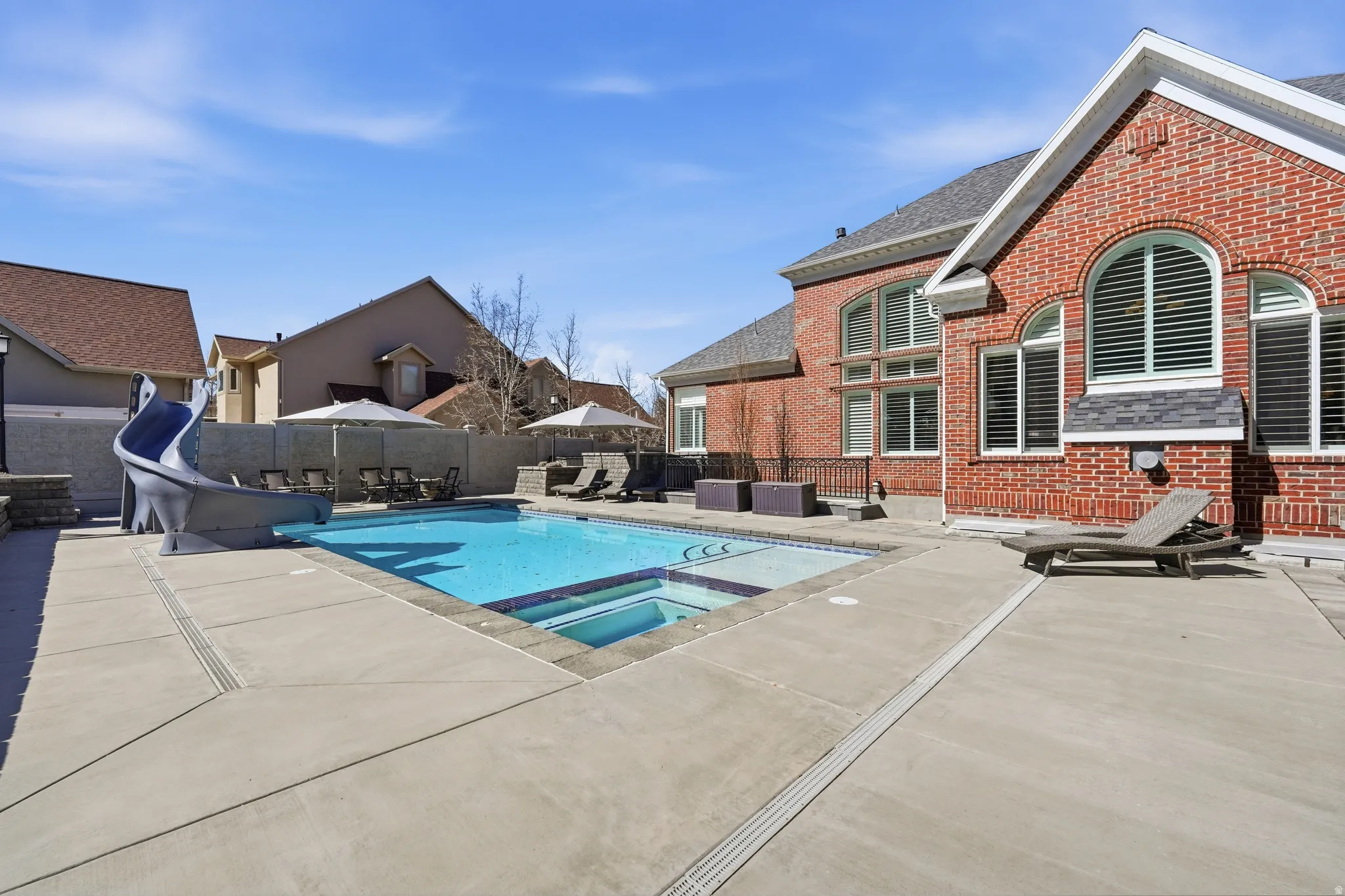 Relaxing pool / spa featuring a water slide, a patio, and a fenced backyard