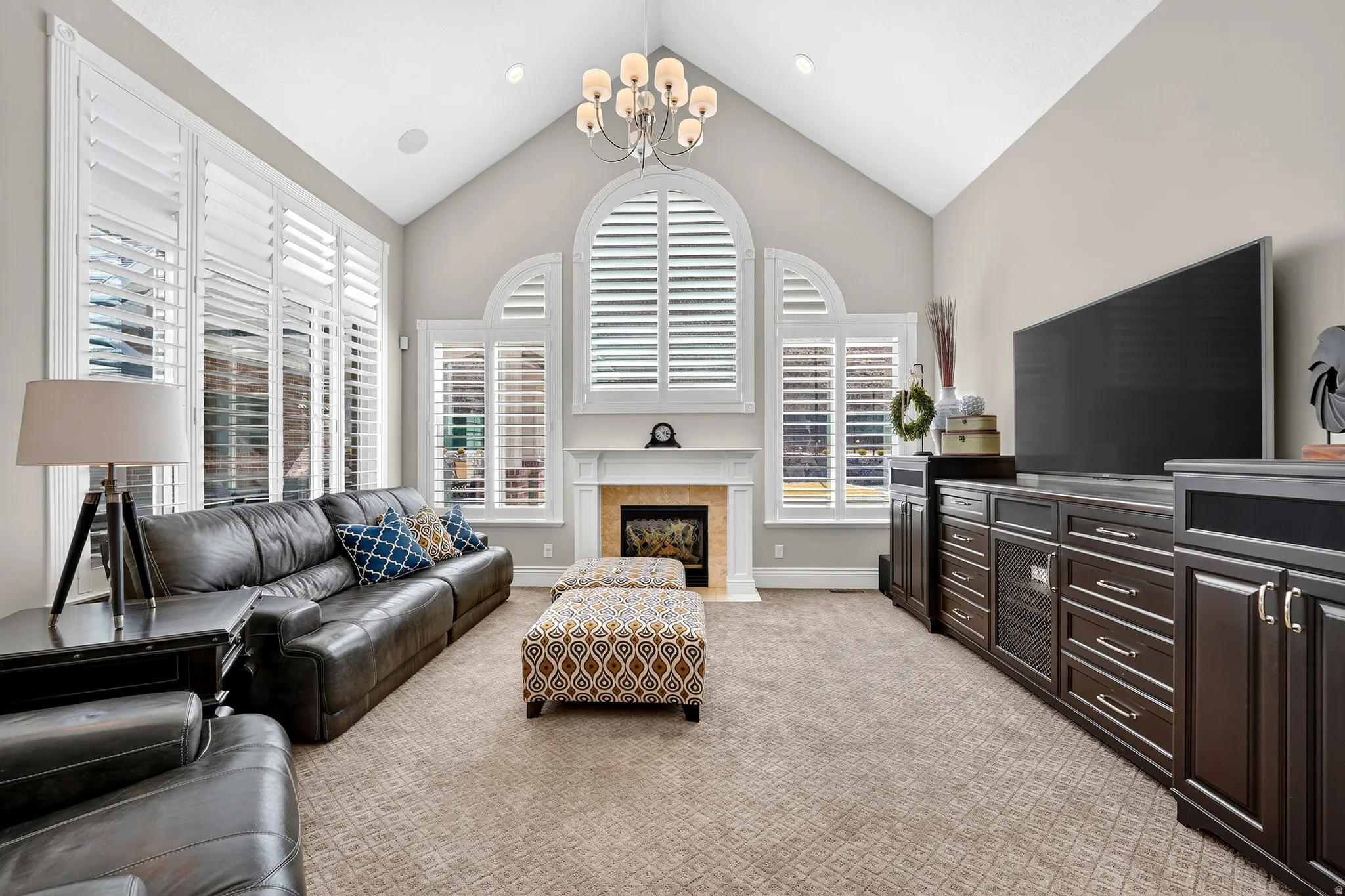 Living area with a high ceiling, light colored carpet, healthy amount of natural light, and a chandelier