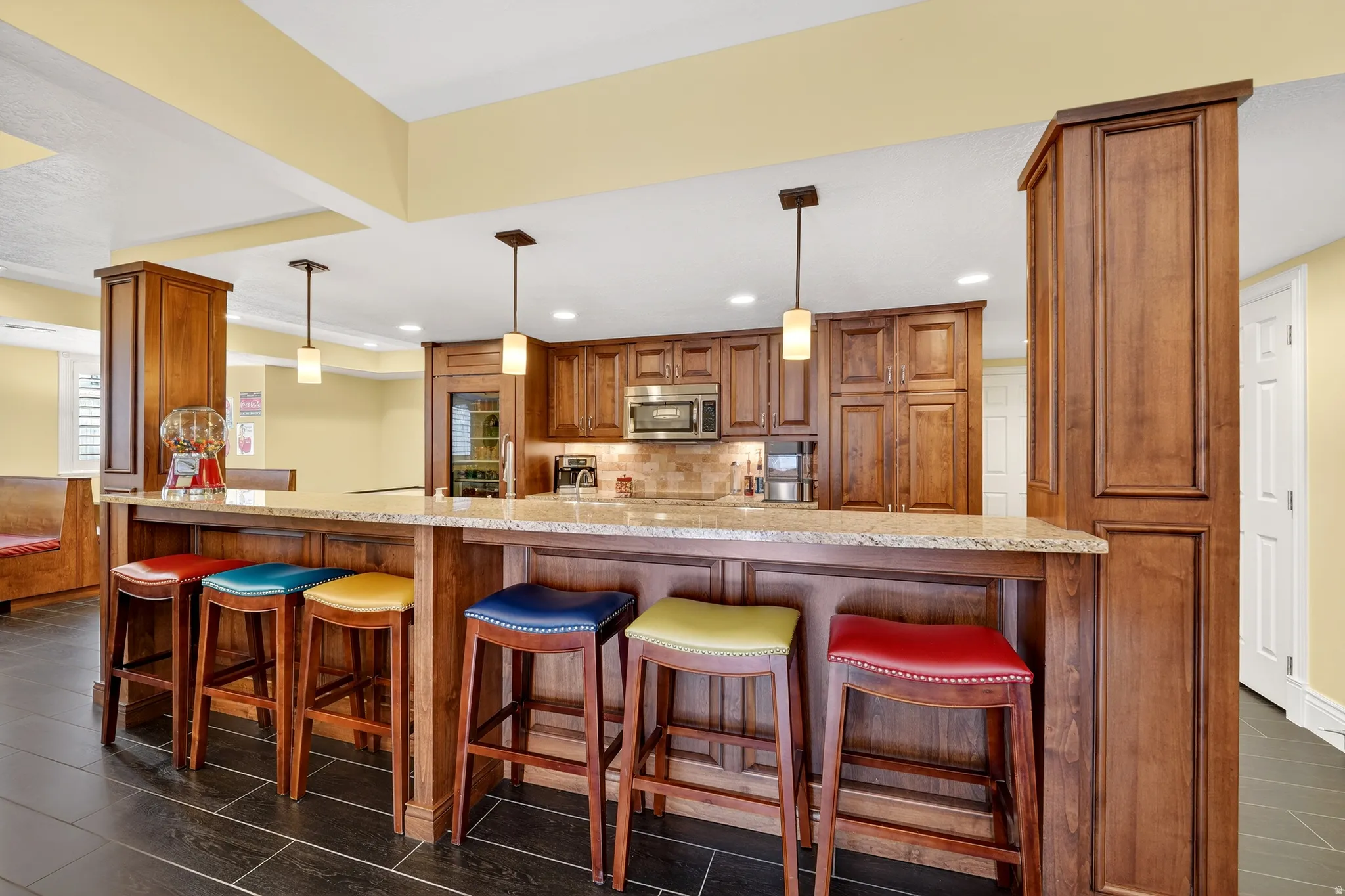 Kitchen with wood finish cabinets, a kitchen bar, hanging light fixtures, light stone counters, and backsplash