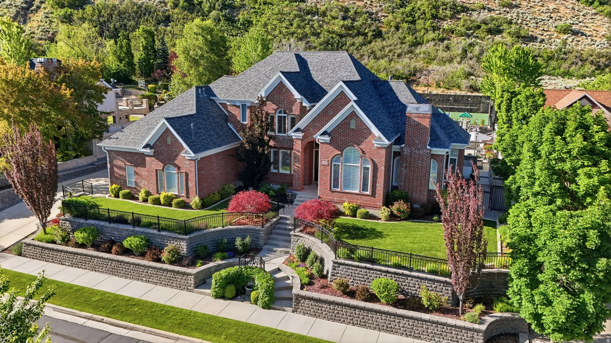 Traditional brick residence featuring a multi-gabled roofline, arched windows, and a landscaped front yard with terraced retaining walls