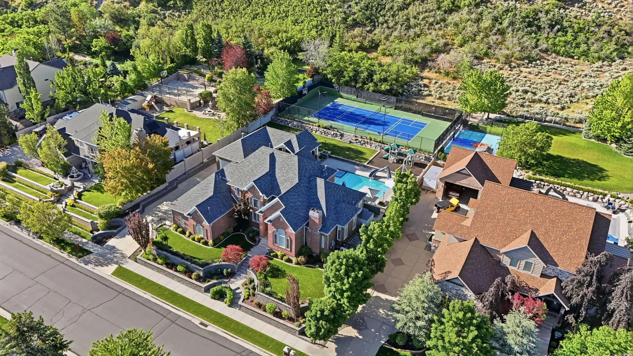 Expansive estate featuring a large main residence with brick and siding exterior, a multi-sport court, a swimming pool, and mature landscaping