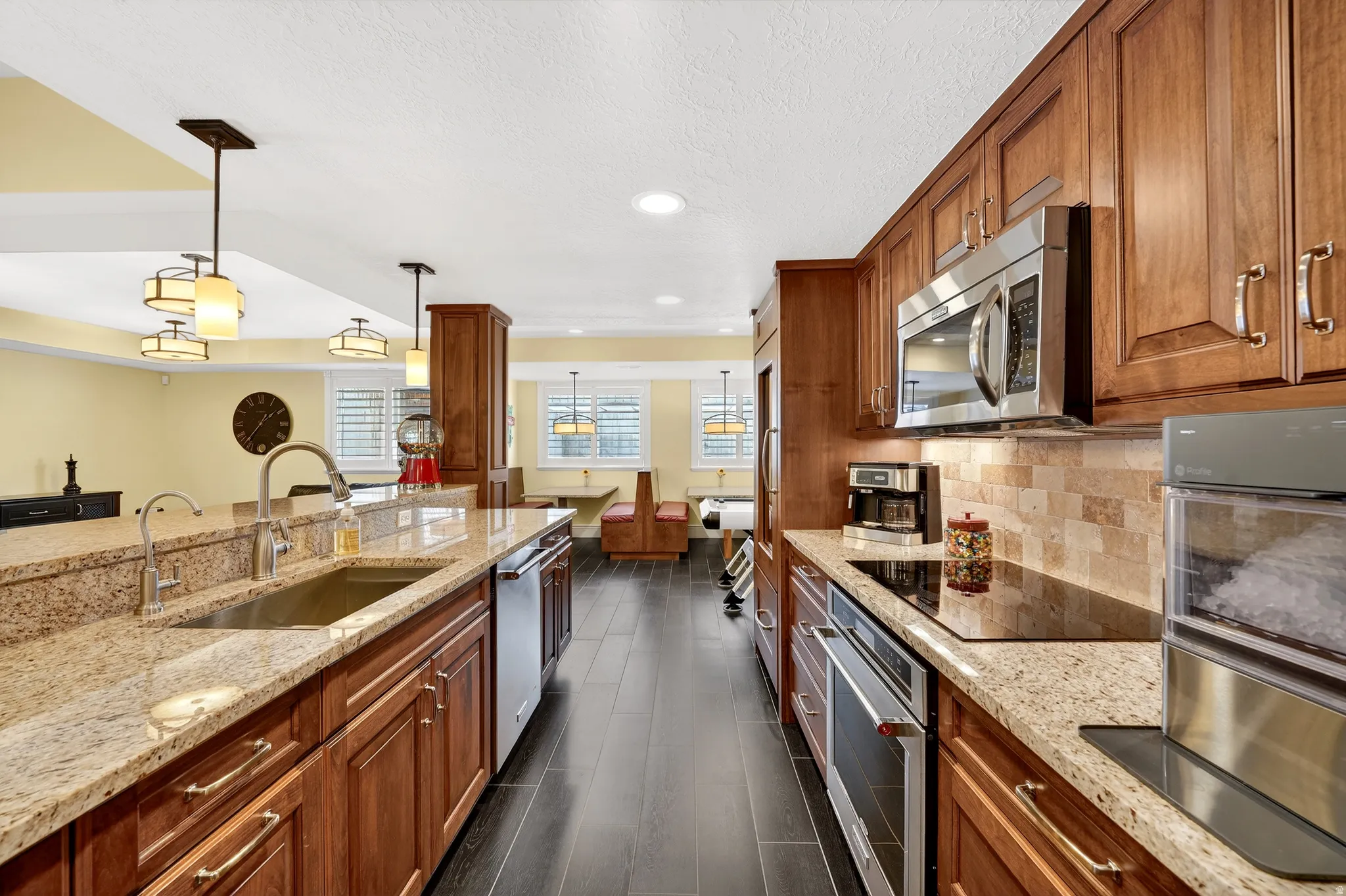 Kitchen featuring wood finish cabinets, light stone counters, stainless steel appliances, pendant lighting, and dark wood-style flooring