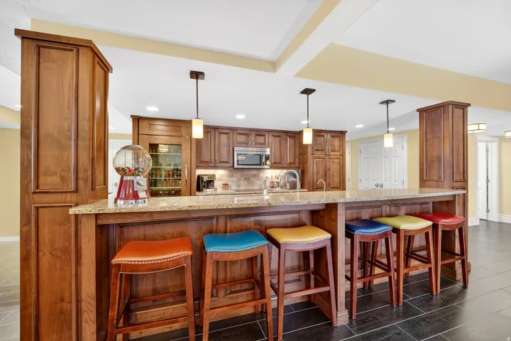 Kitchen with wood finish cabinetry, a breakfast bar area, a peninsula, light stone counters, and pendant lighting