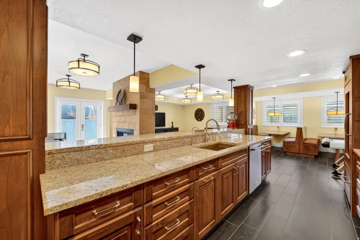 Kitchen with wood finish cabinetry, light stone counters, hanging light fixtures, a fireplace, and a textured ceiling