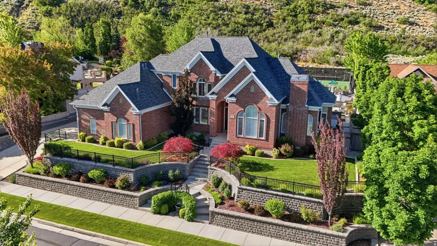Traditional brick residence featuring a multi-gabled roofline, arched windows, and a landscaped front yard with terraced retaining walls