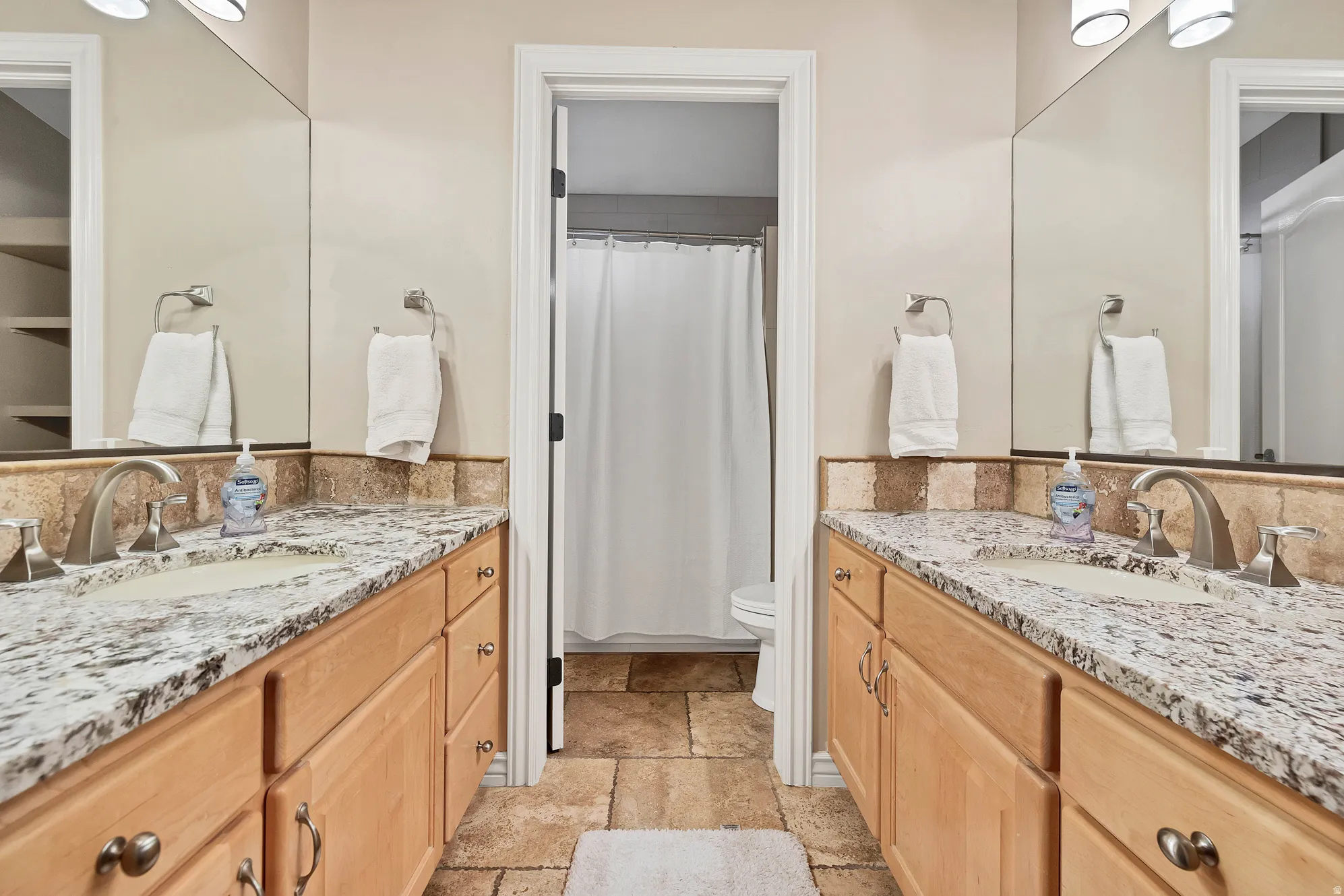 Bathroom with two vanities, stone tile floors, and a shower with curtain