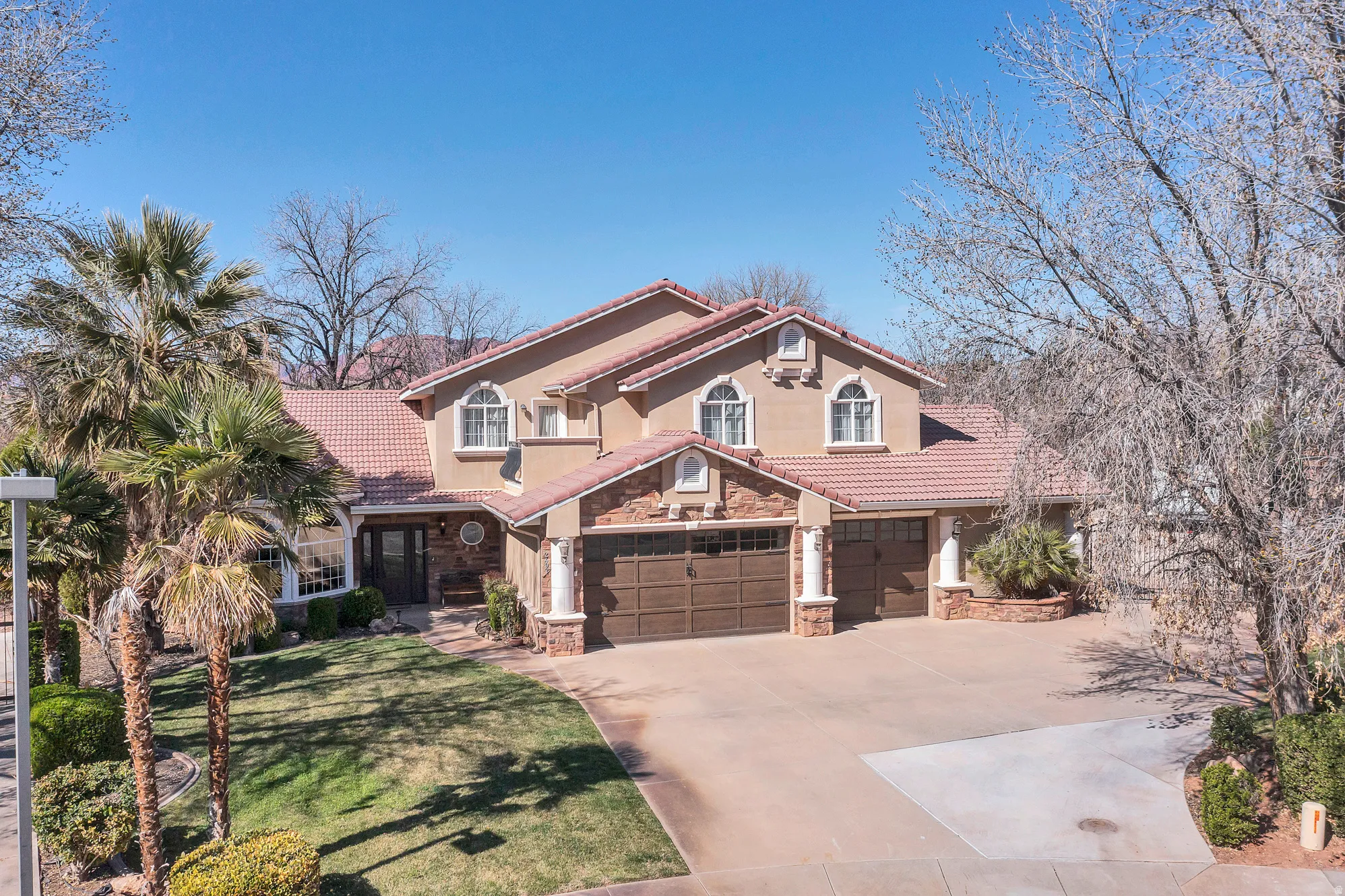 Mediterranean / spanish home featuring a tiled roof, concrete driveway, stone siding, a front lawn, and an attached garage