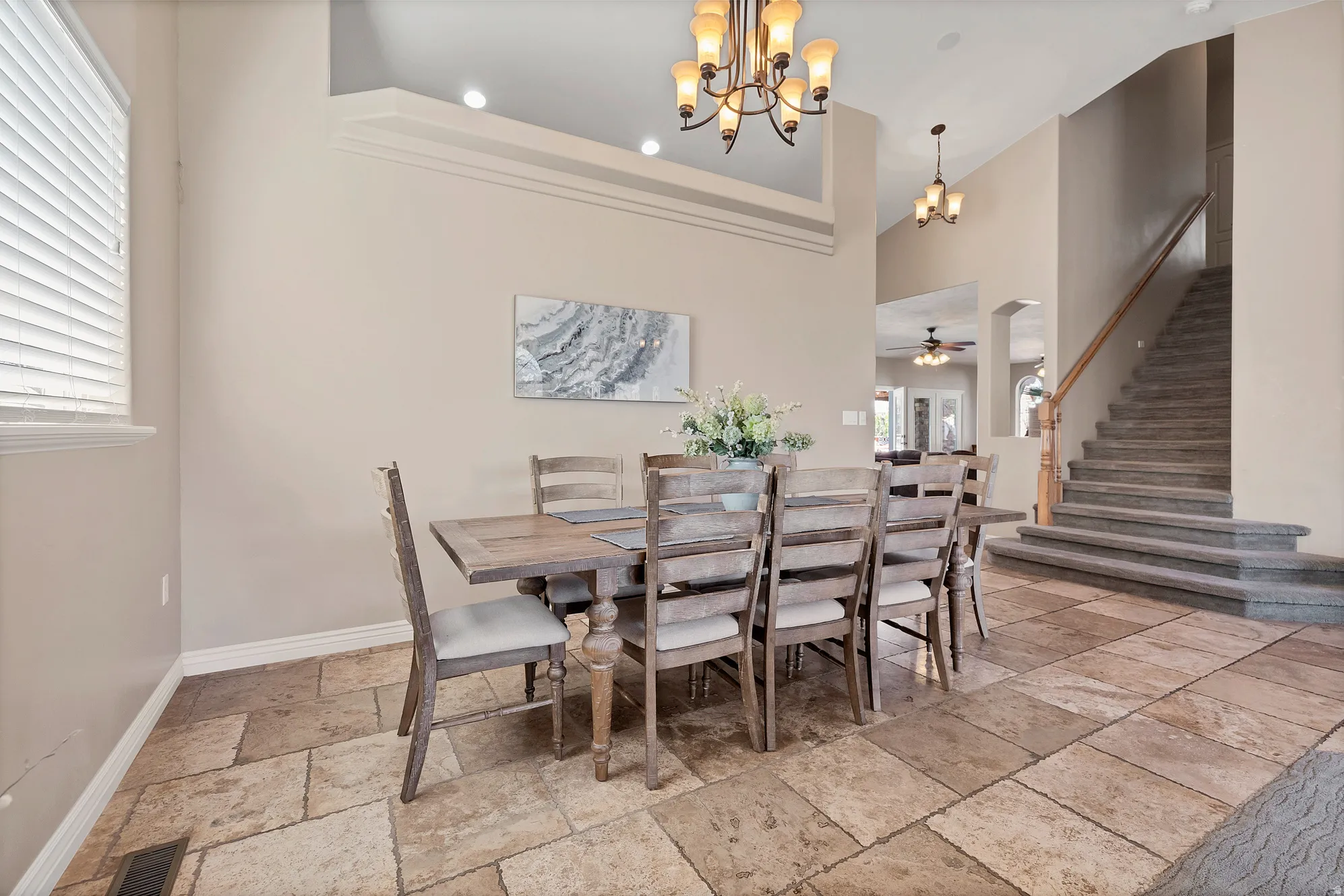 Dining space featuring stone tile floors, hanging lights, ceiling fan, and a high ceiling