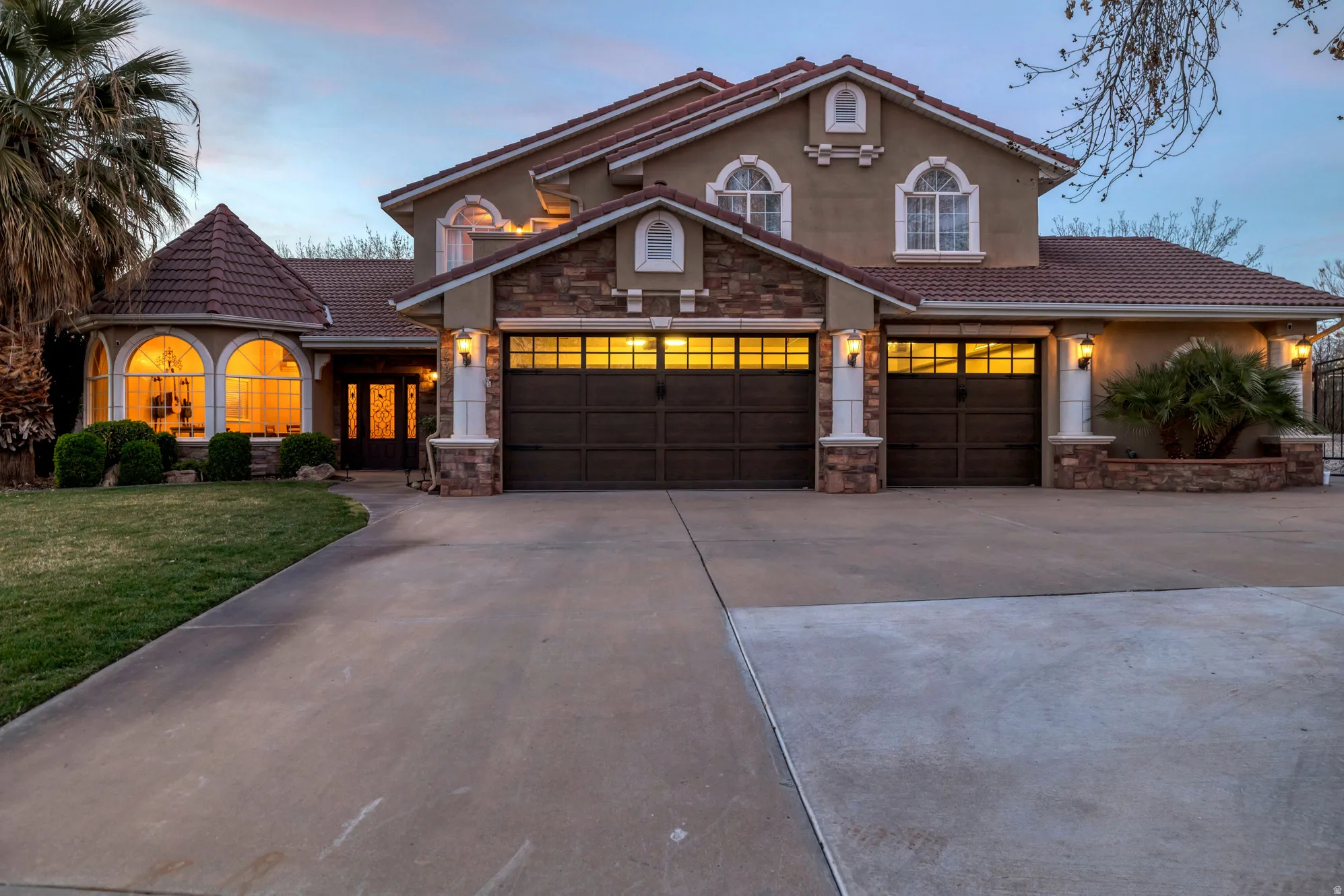 Mediterranean / spanish home featuring stone siding, driveway, stucco siding, a tile roof, and a front yard