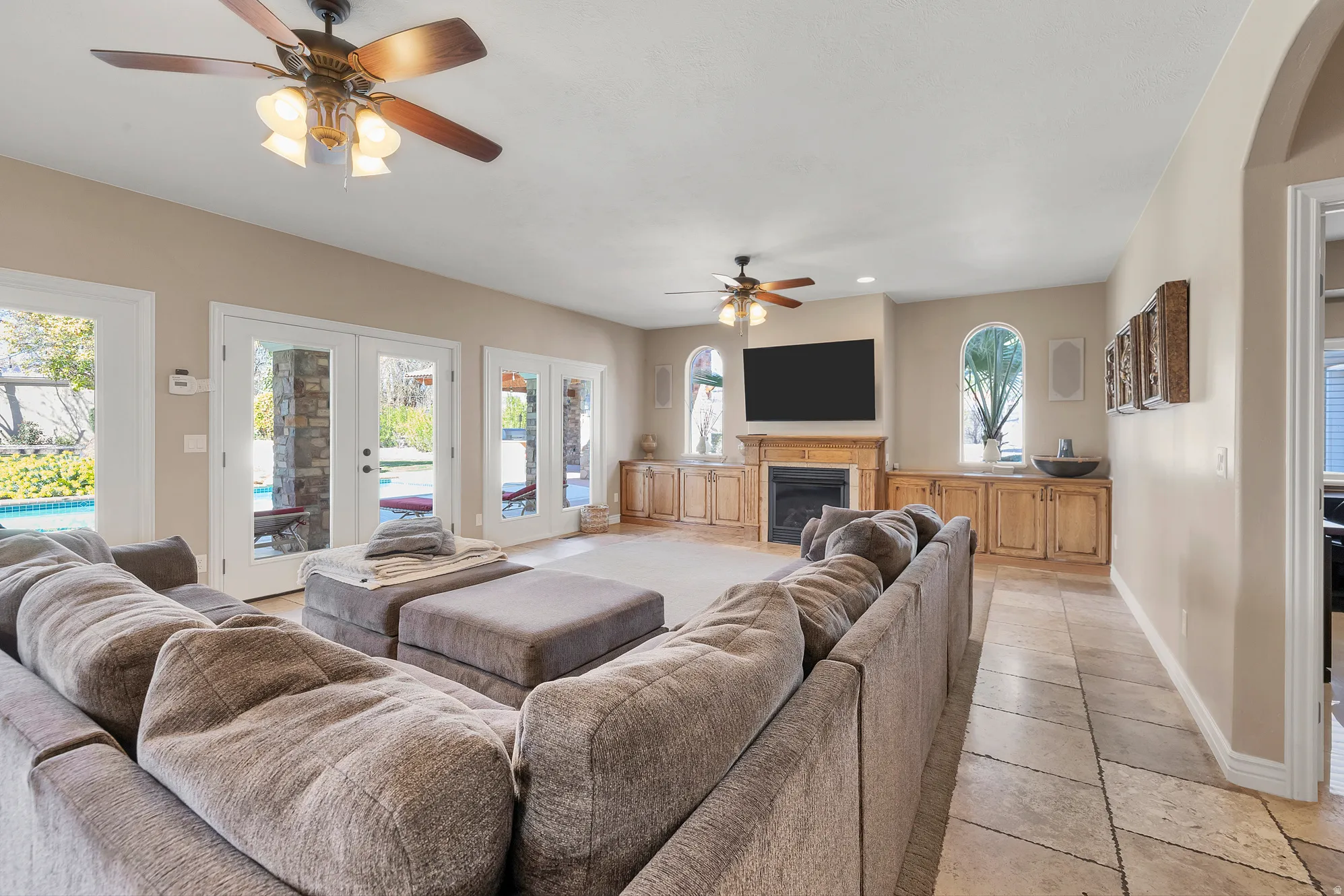 Living room featuring french doors, a ceiling fan, a glass covered fireplace, and arched walkways
