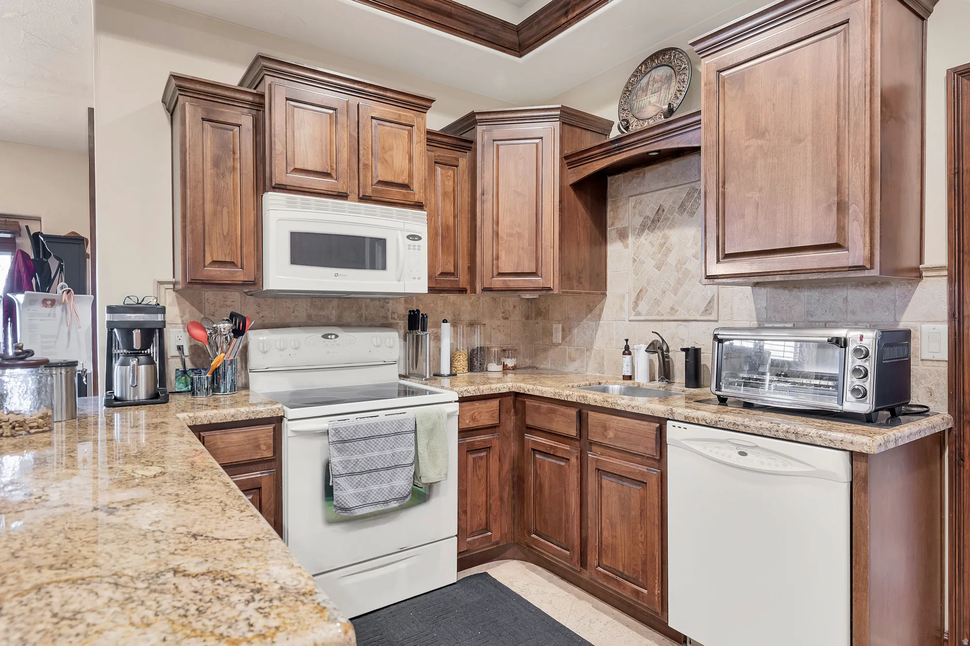 Kitchen featuring white appliances, light stone counters, wood finish cabinetry, and tasteful backsplash