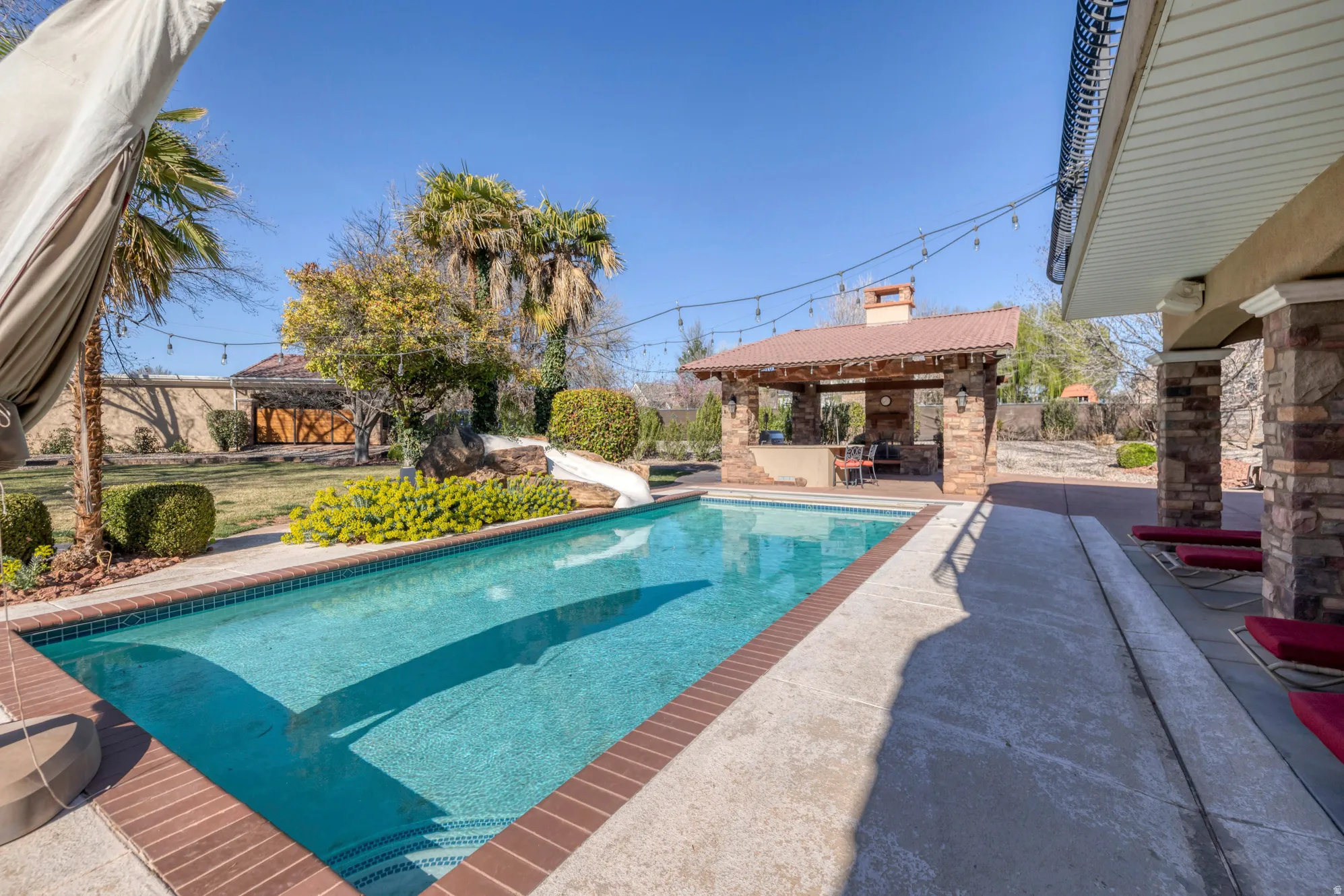 View of swimming pool with patio surround, a water slide, a fenced backyard, and exterior bar