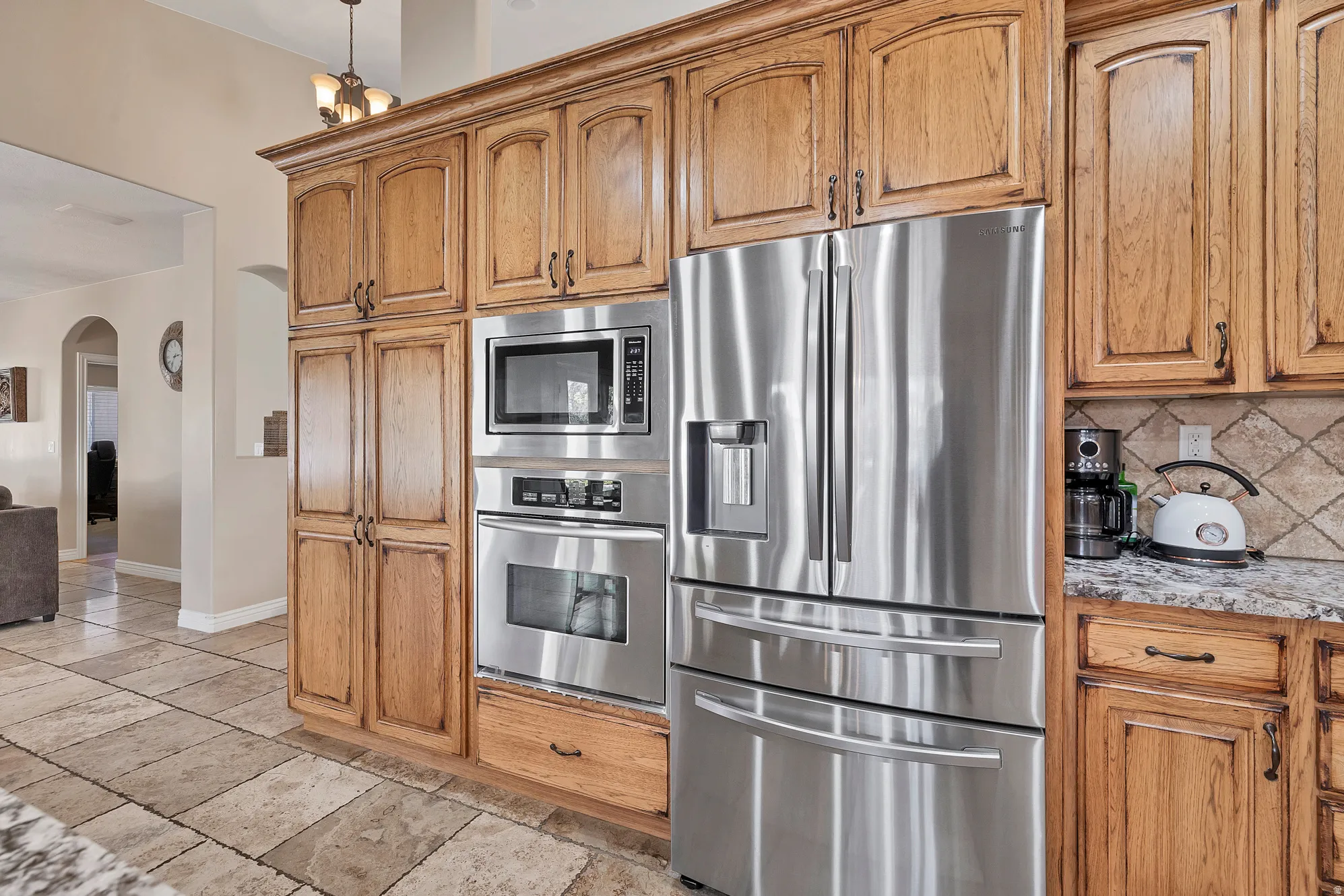 Kitchen featuring stainless steel appliances, arched walkways, decorative backsplash, light stone countertops, and wood finish cabinets
