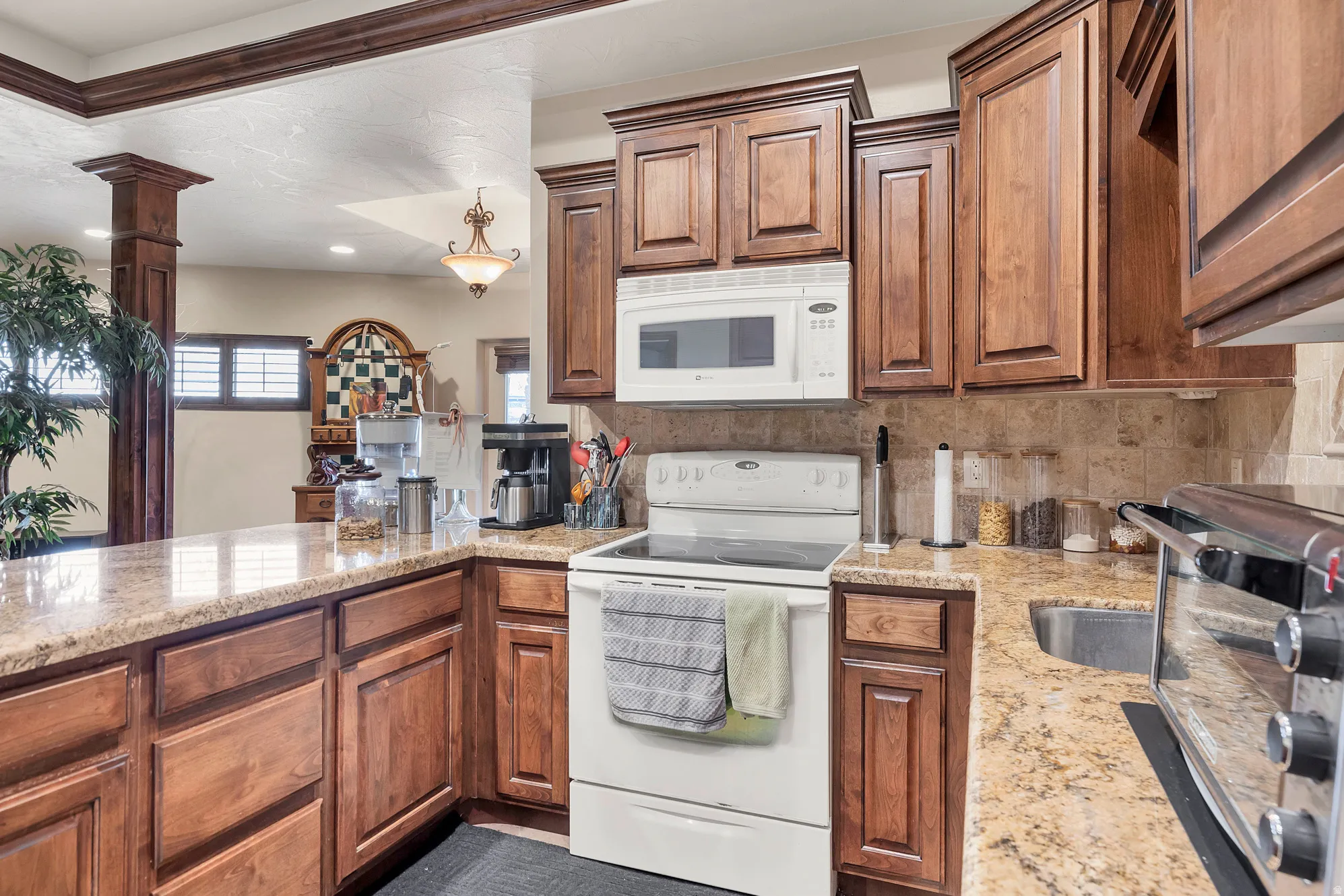 Kitchen featuring white appliances, light stone countertops, wood finish cabinets, and decorative backsplash