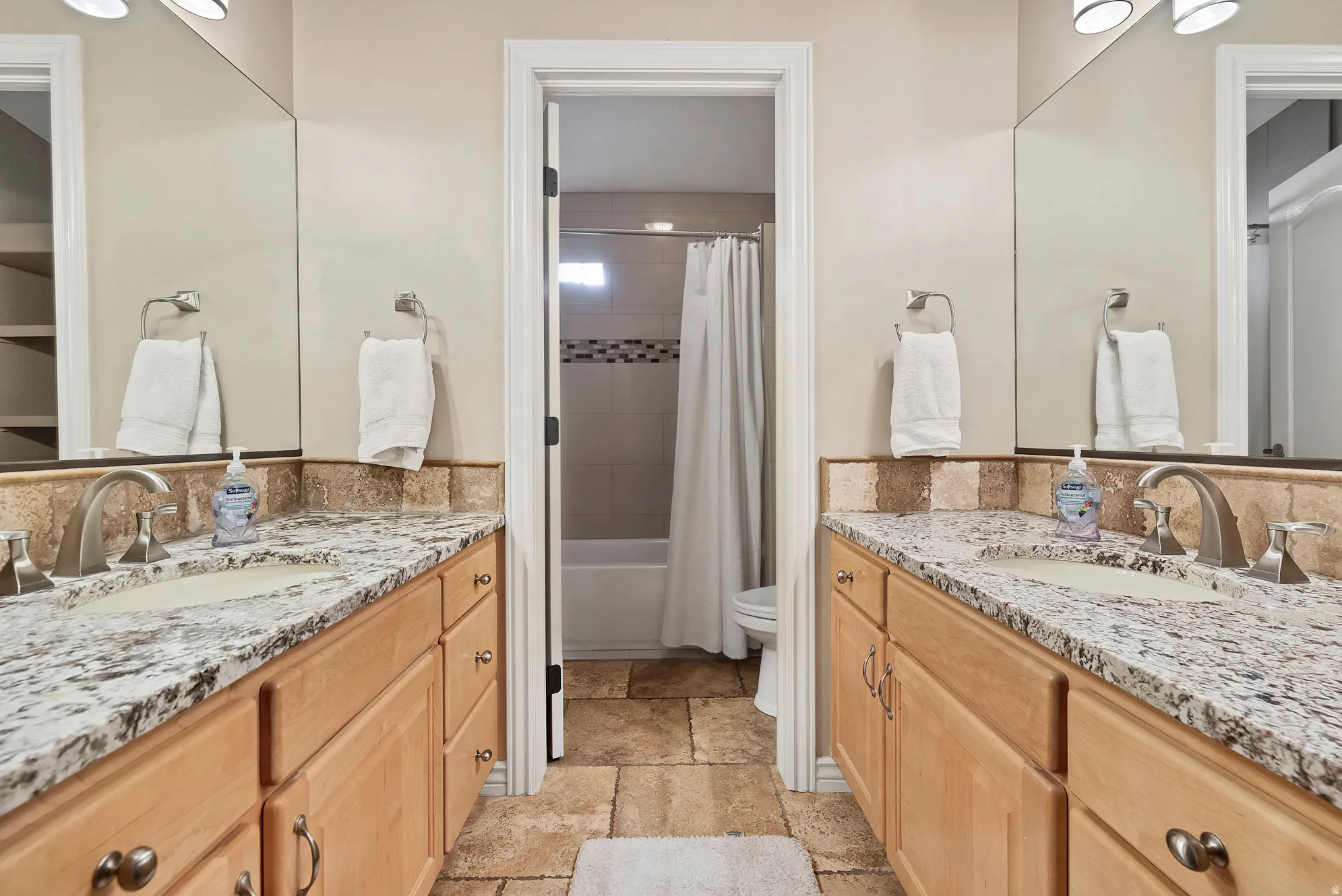 Full bathroom with two vanities, stone tile floors, and shower / tub combo with curtain
