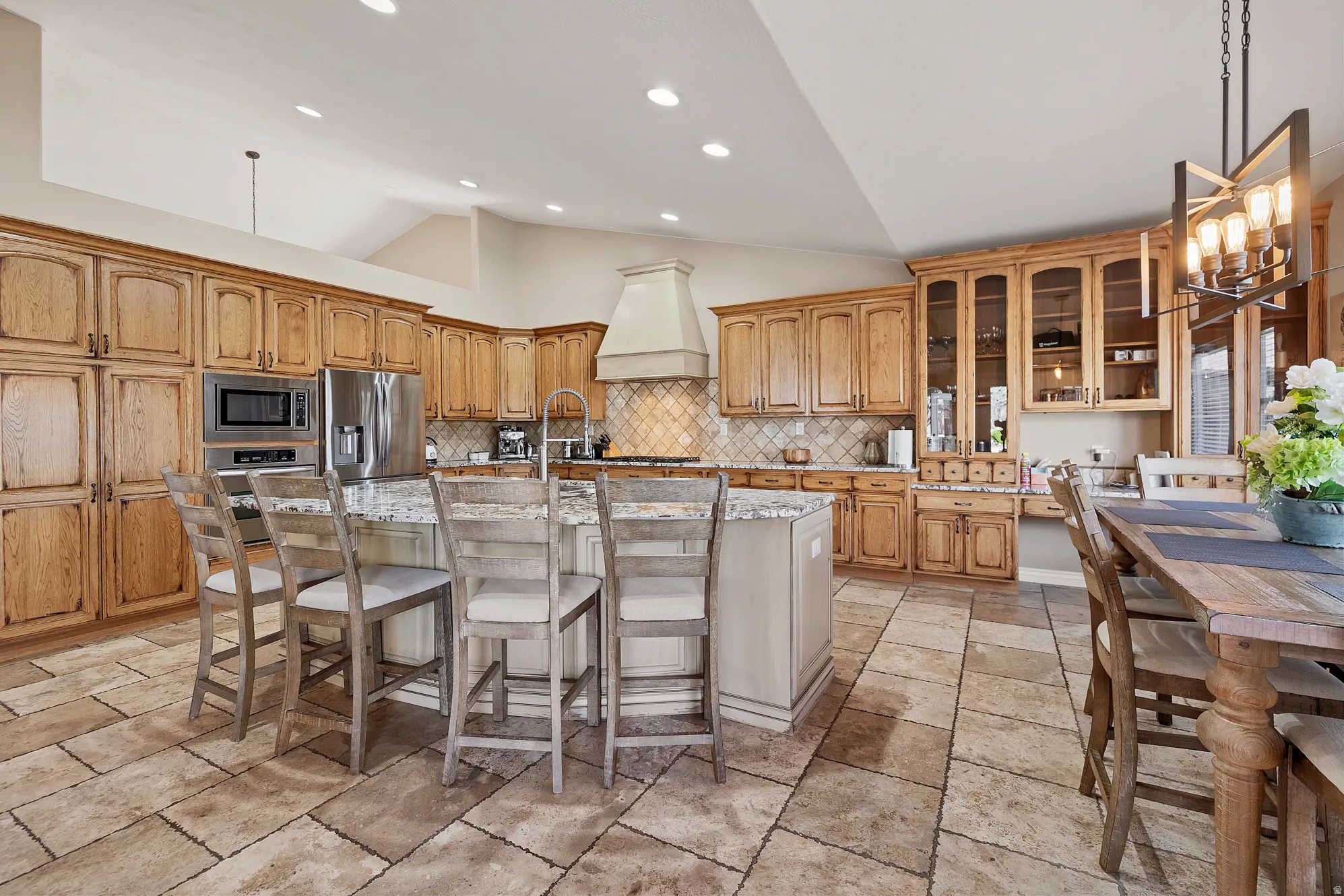 Kitchen featuring vaulted ceiling, a kitchen island with sink, a kitchen breakfast bar, glass fronted cabinets, and stainless steel appliances