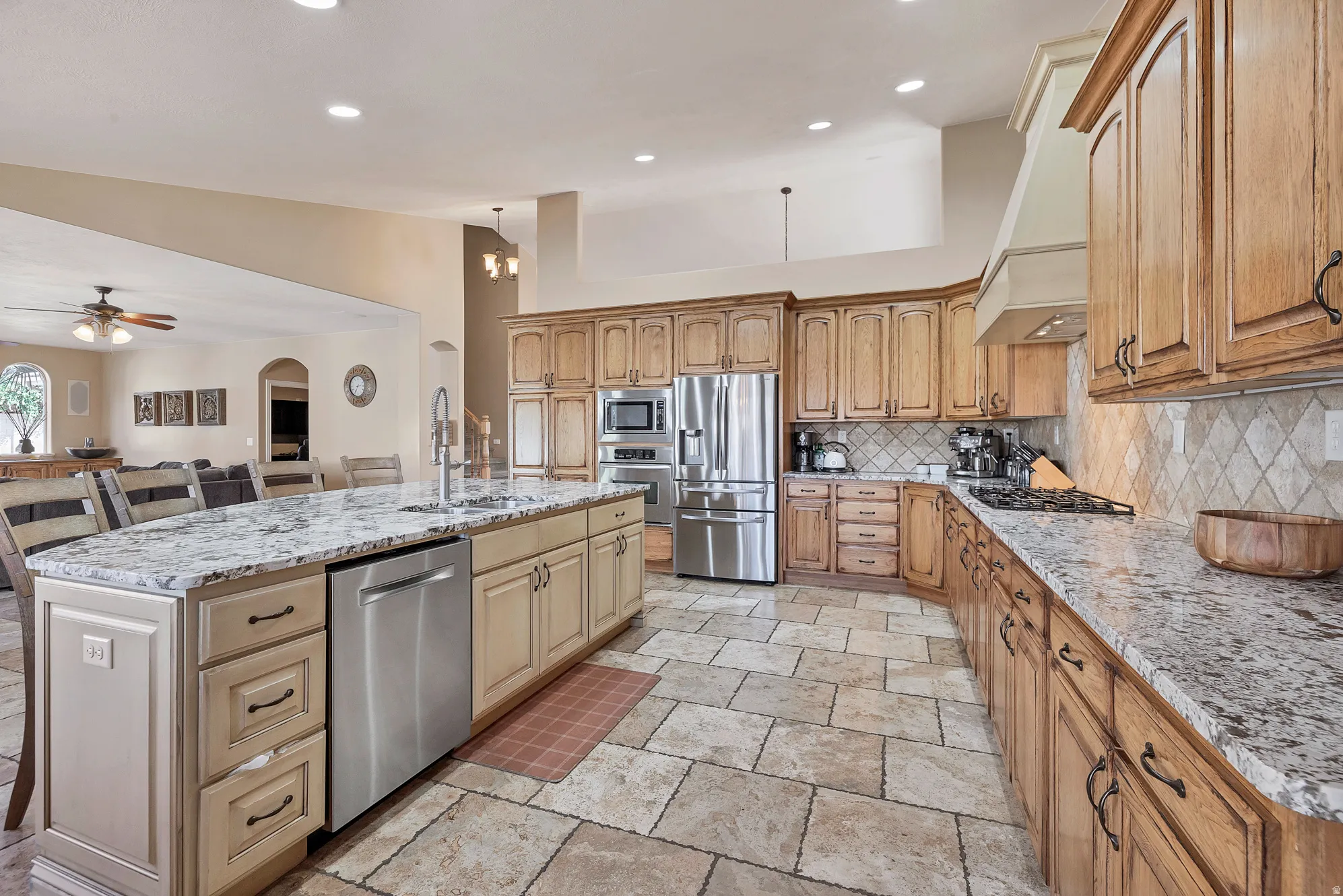 Kitchen featuring a kitchen island with sink, stainless steel appliances, light stone countertops, ceiling fan, and backsplash