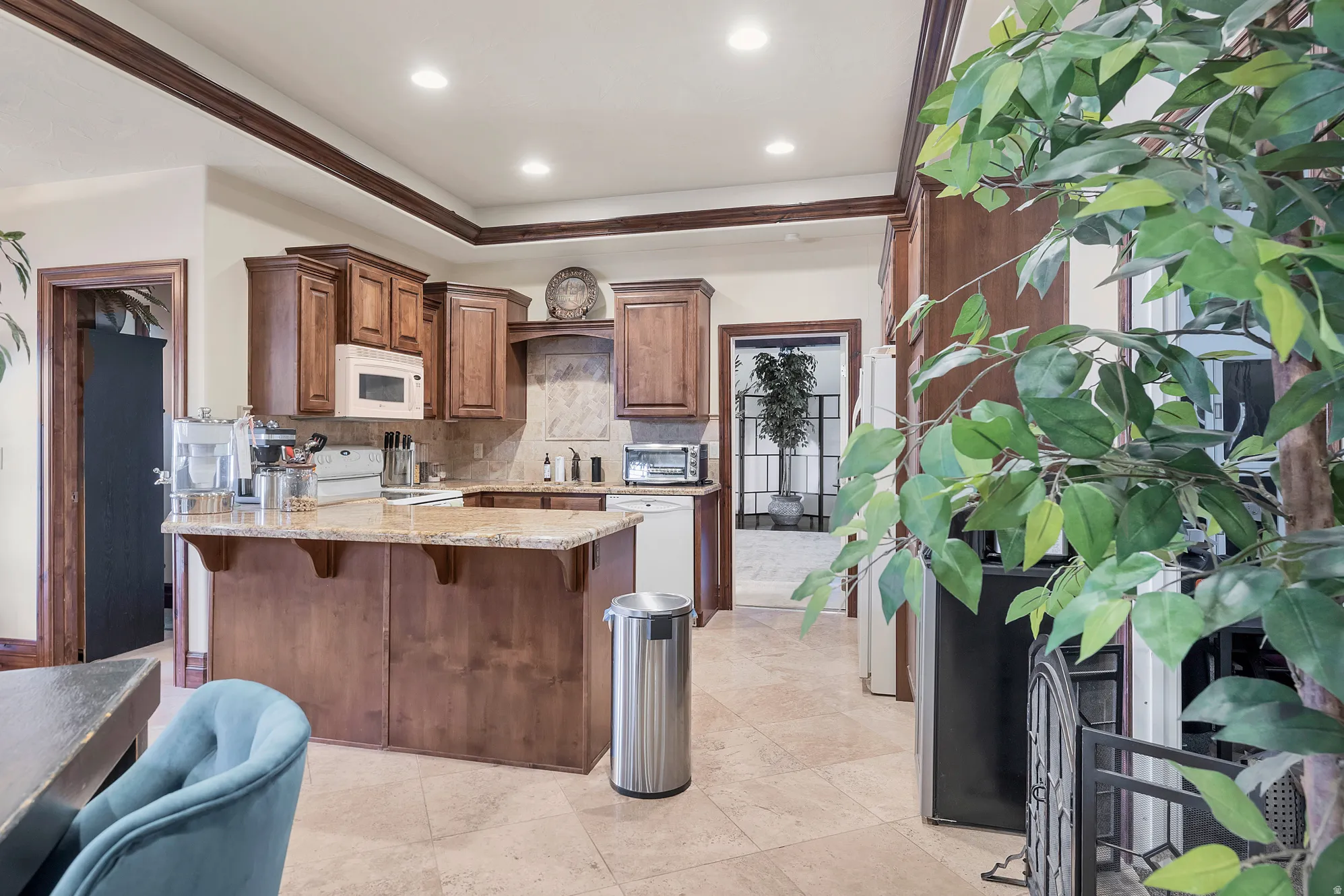 Kitchen featuring a kitchen breakfast bar, light stone countertops, backsplash, white appliances, and a peninsula