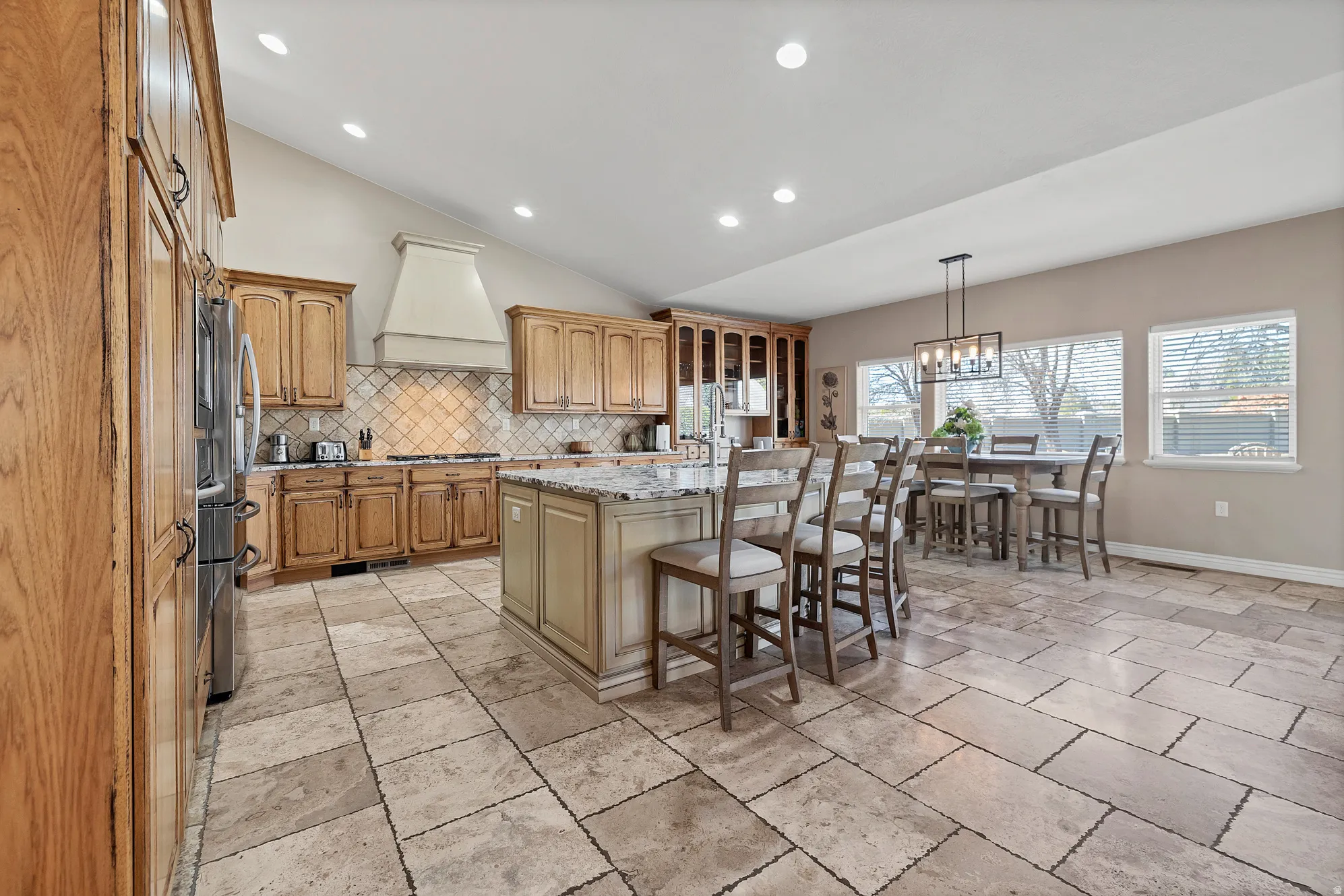 Kitchen featuring a breakfast bar area, vaulted ceiling, a kitchen island, light stone countertops, and glass fronted cabinets