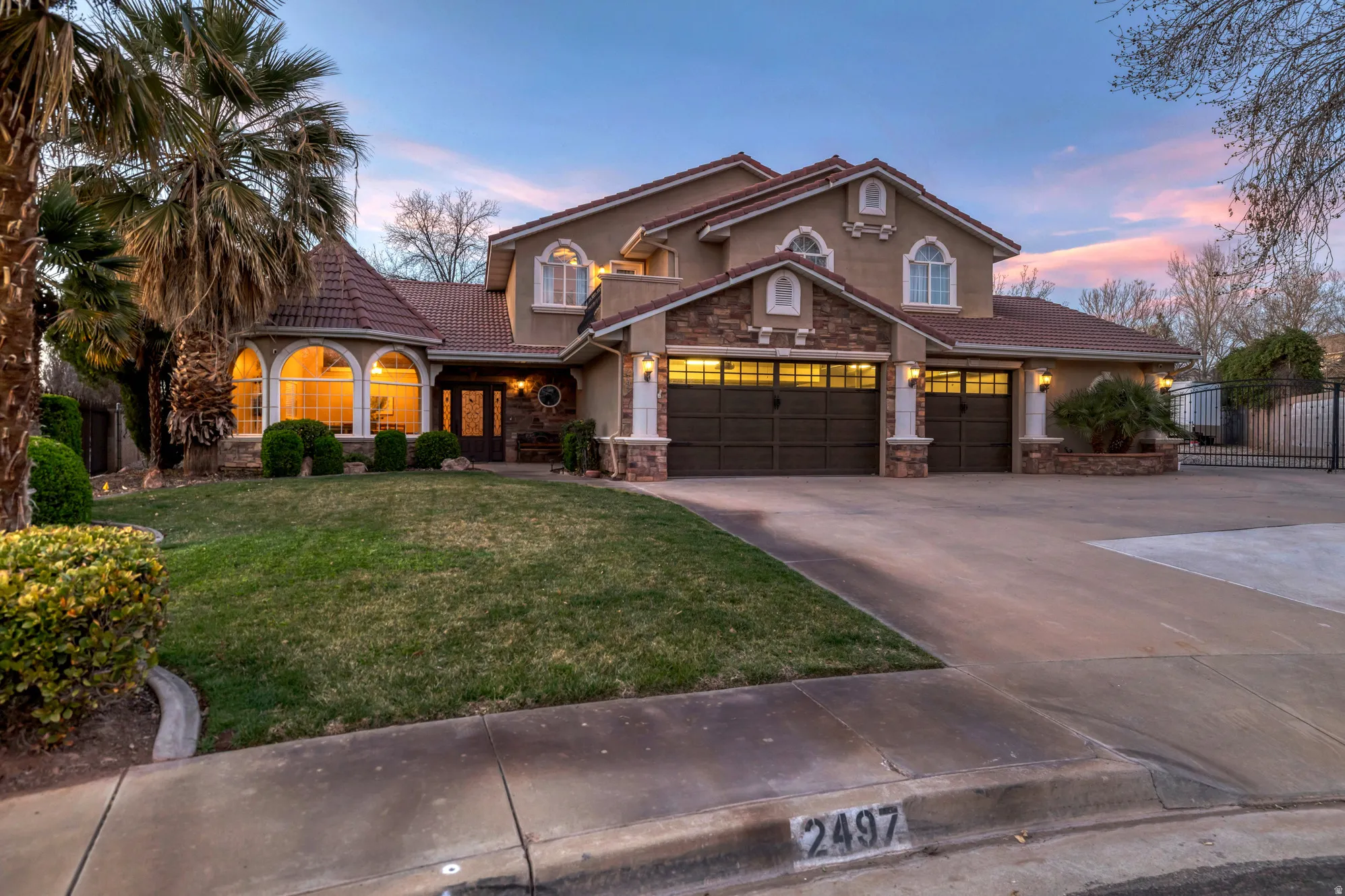 Mediterranean / spanish-style house featuring a tiled roof, stone siding, a front yard, driveway, and stucco siding