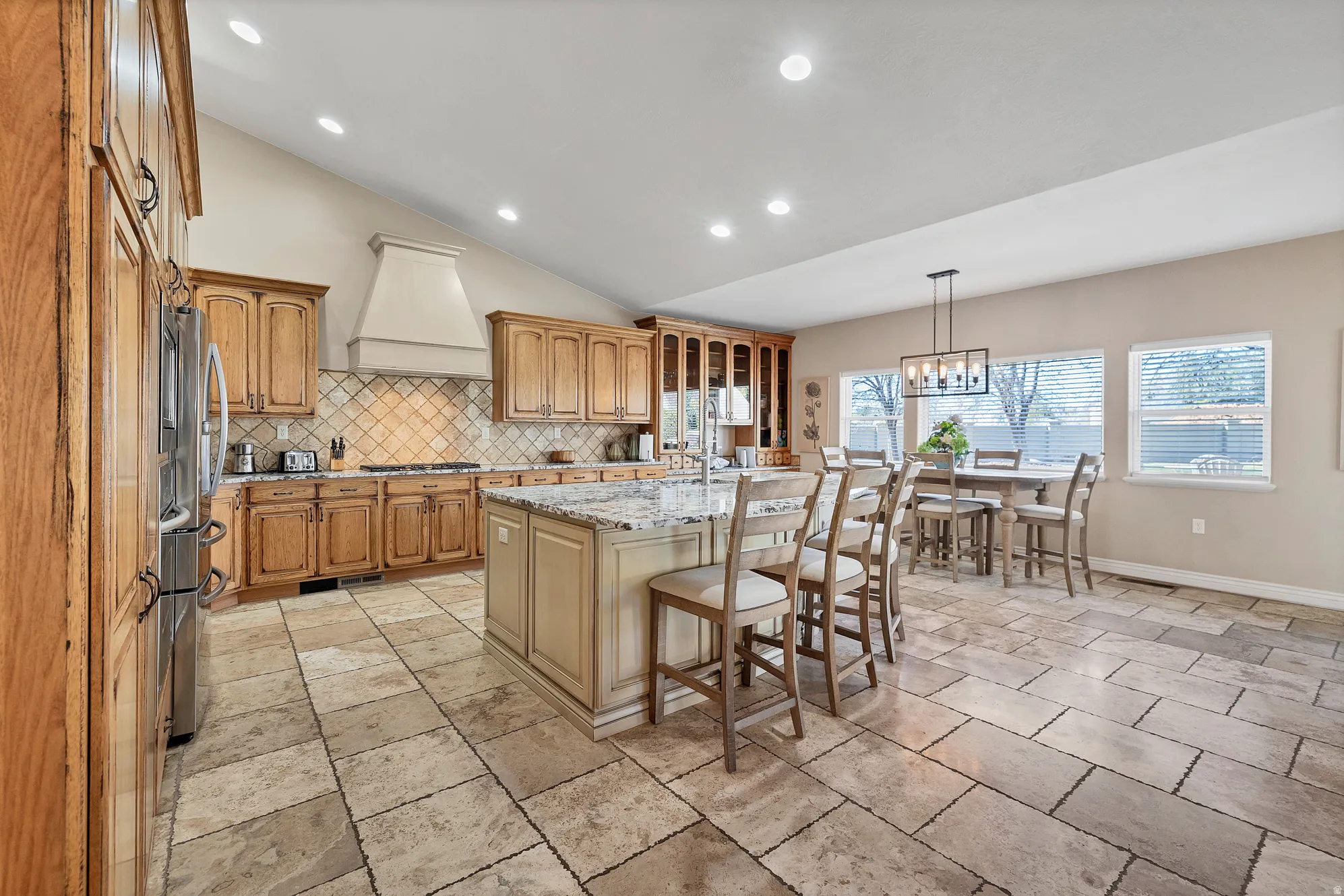 Kitchen featuring a breakfast bar, lofted ceiling, light stone counters, a center island with sink, and stainless steel appliances