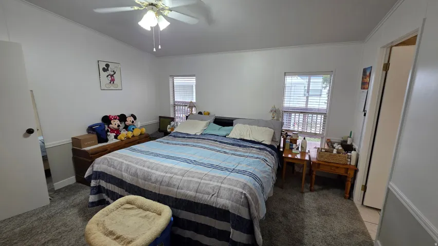 Bedroom featuring light colored carpet, multiple windows, a ceiling fan, vaulted ceiling, and ornamental molding
