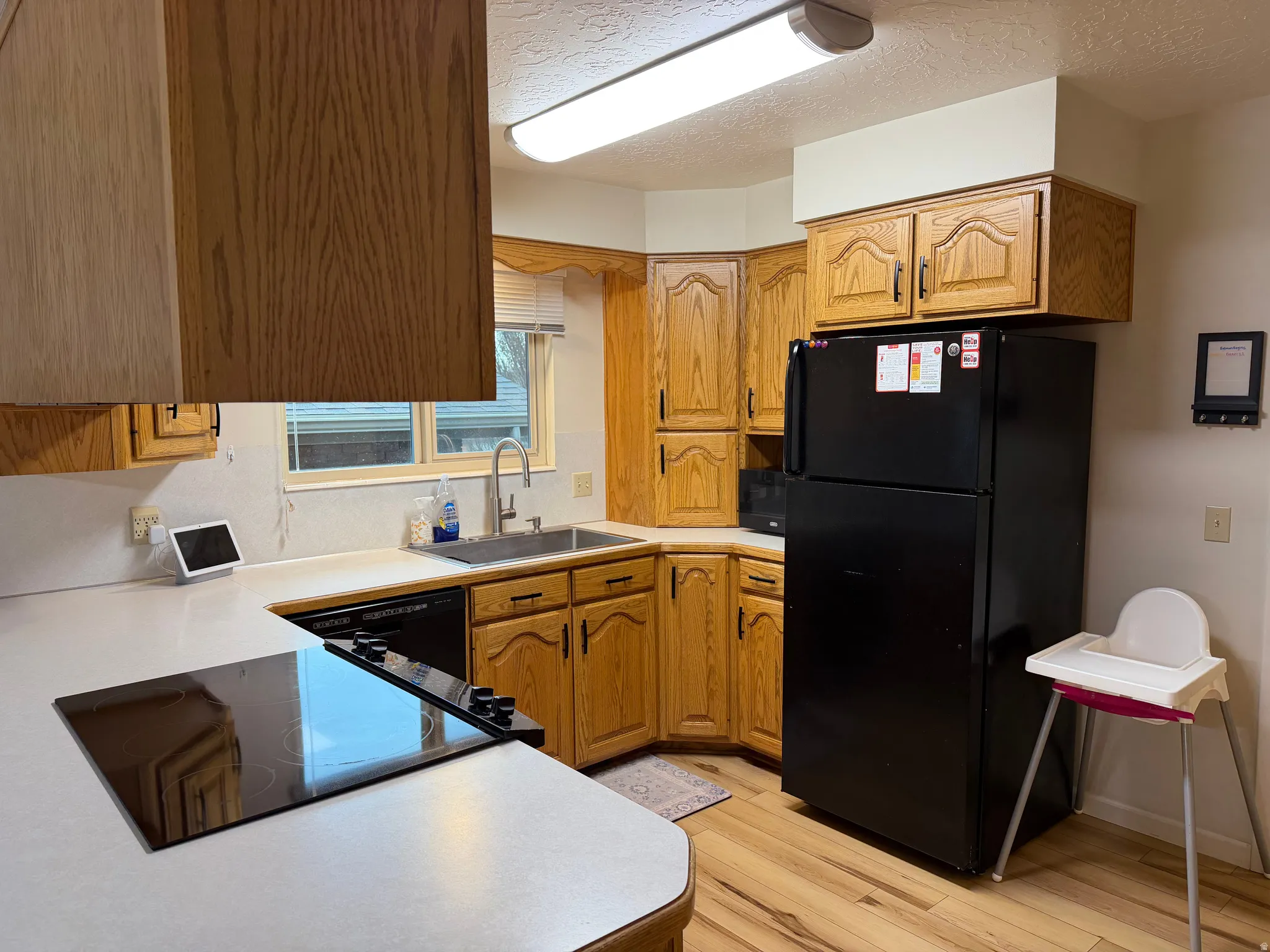 Kitchen with black appliances, a textured ceiling, light countertops, light wood-type flooring, and wood finish cabinets