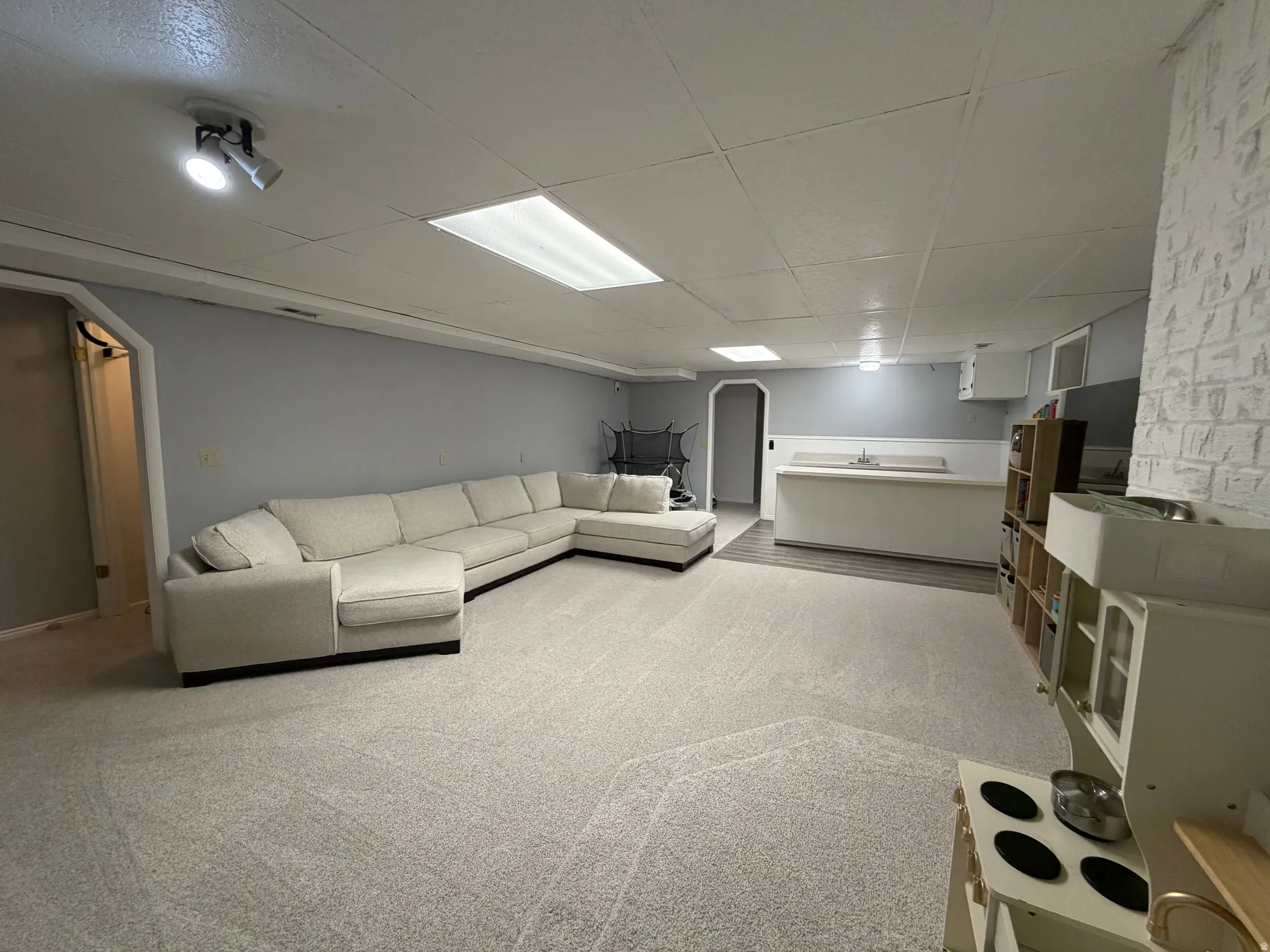 Living area featuring arched walkways, light carpet, and a drop ceiling