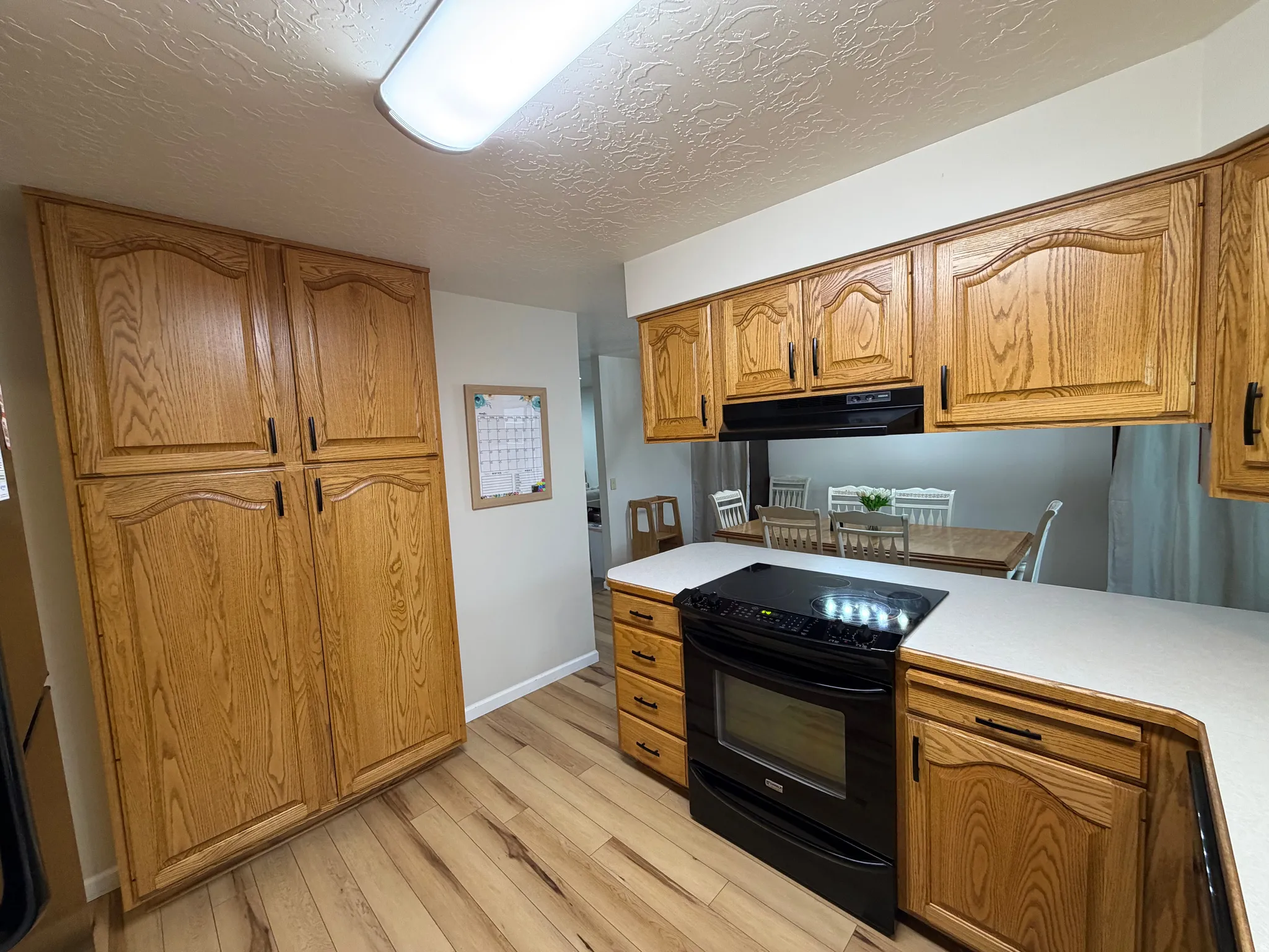 Kitchen featuring black / electric stove, light countertops, a textured ceiling, light wood-type flooring, and wood finish cabinetry