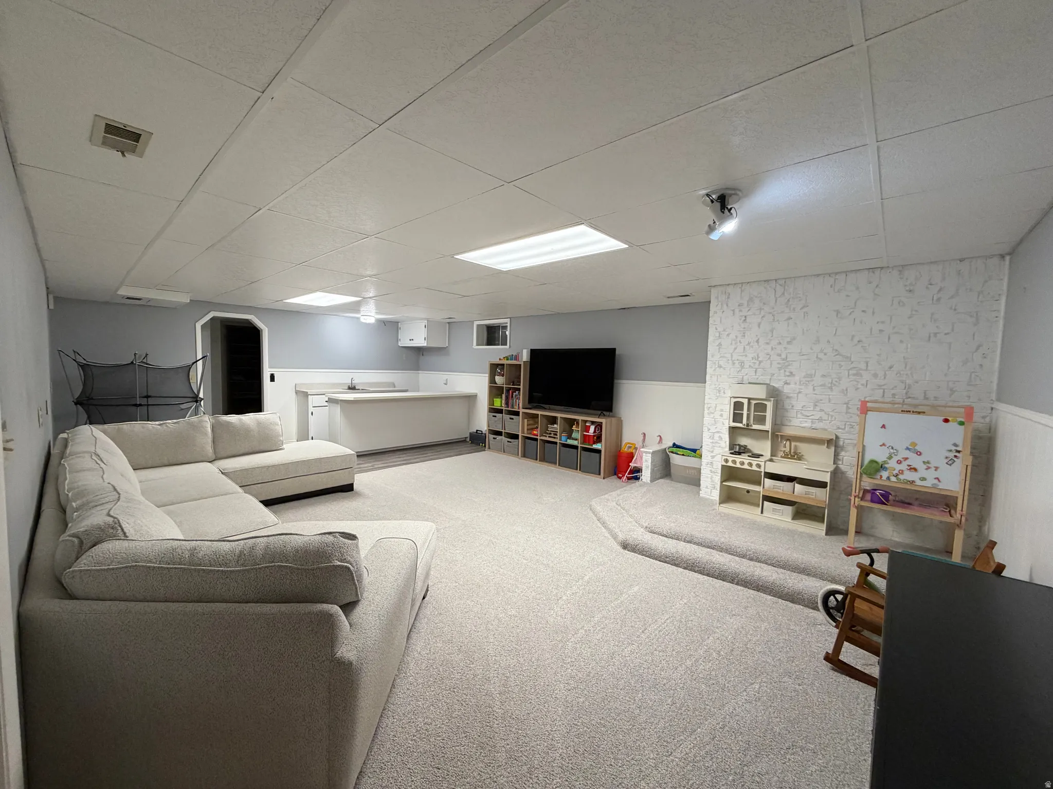 Living area with a drop ceiling, wainscoting, and carpet floors
