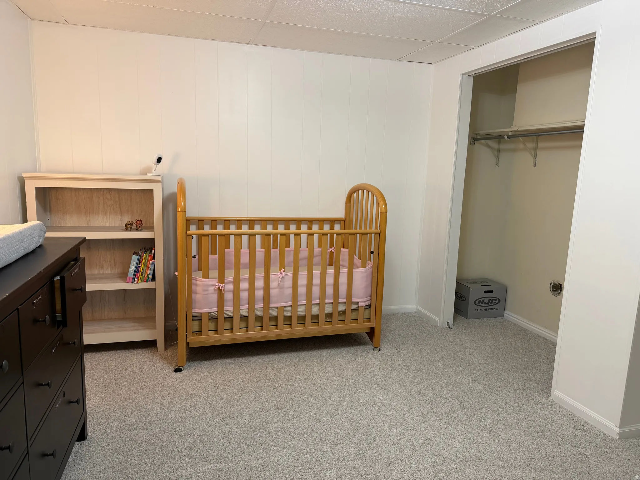 Bedroom with light carpet, a drop ceiling, a closet, and a crib