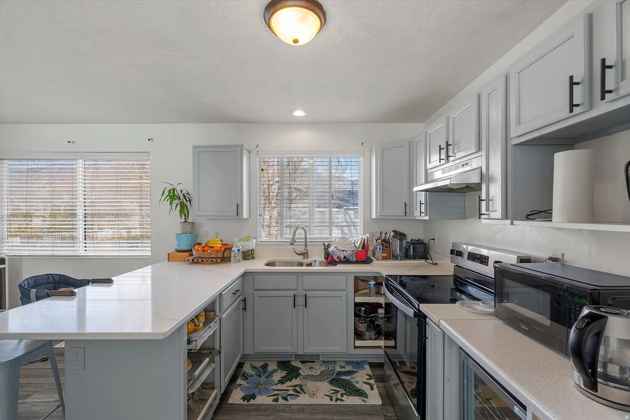Kitchen featuring a peninsula, gray cabinets, electric range, black microwave, and a breakfast bar area