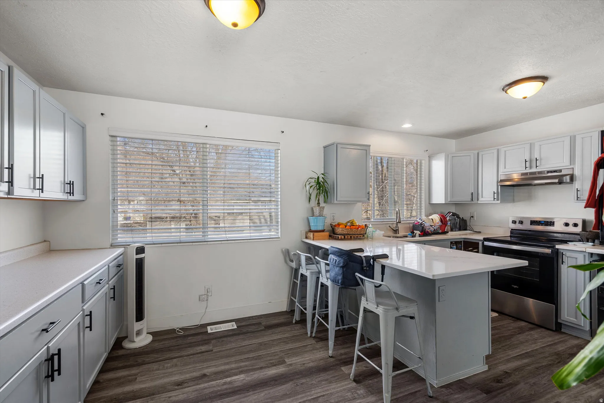 Kitchen featuring stainless steel range with electric stovetop, a breakfast bar, a peninsula, dark wood-style flooring, and gray cabinets