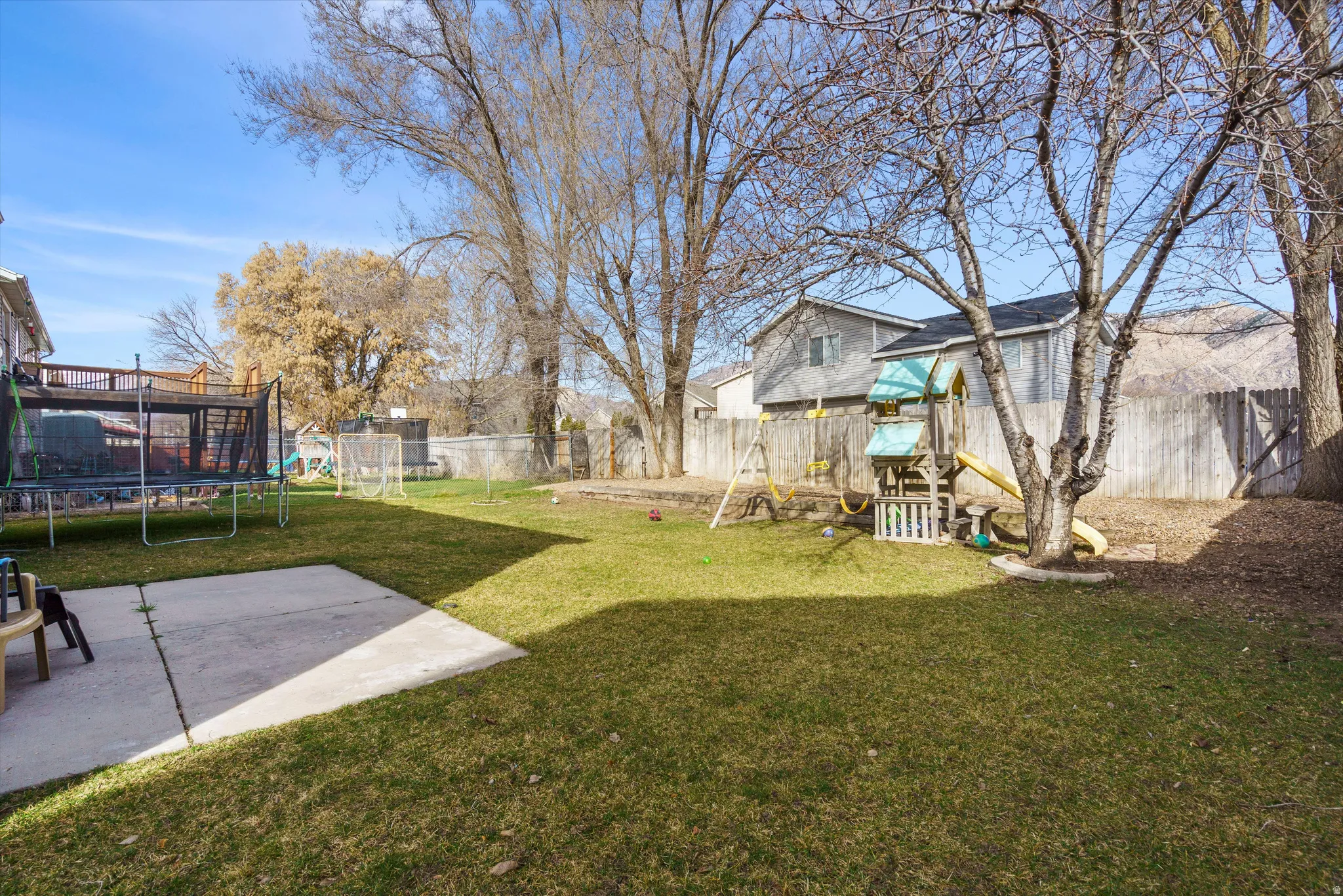 Fenced backyard featuring a trampoline and a playground