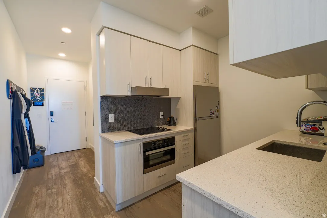 Kitchen featuring light stone counters, freestanding refrigerator, wall oven, light wood-style floors, and backsplash