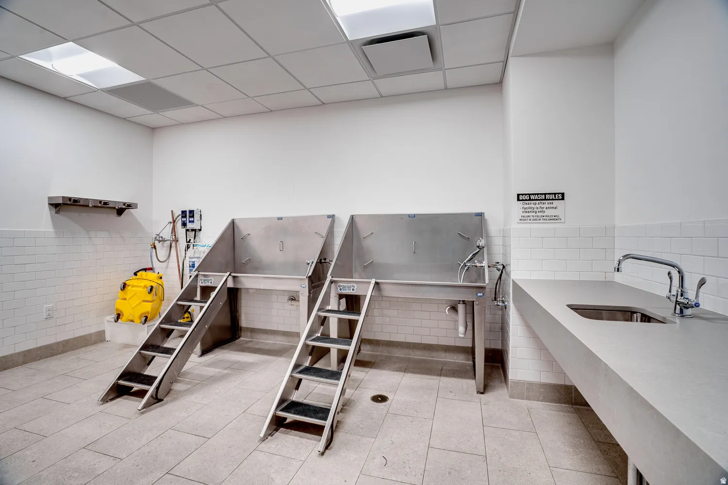 Misc room with a drop ceiling, a wainscoted wall, pet washing station, and tile walls